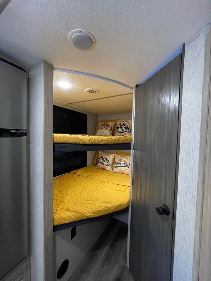 Cozy bunk beds inside an RV rental, featuring yellow bedding & "Adventure Wilderness" pillows for travelers.. Coachmen Freedom Express 2021