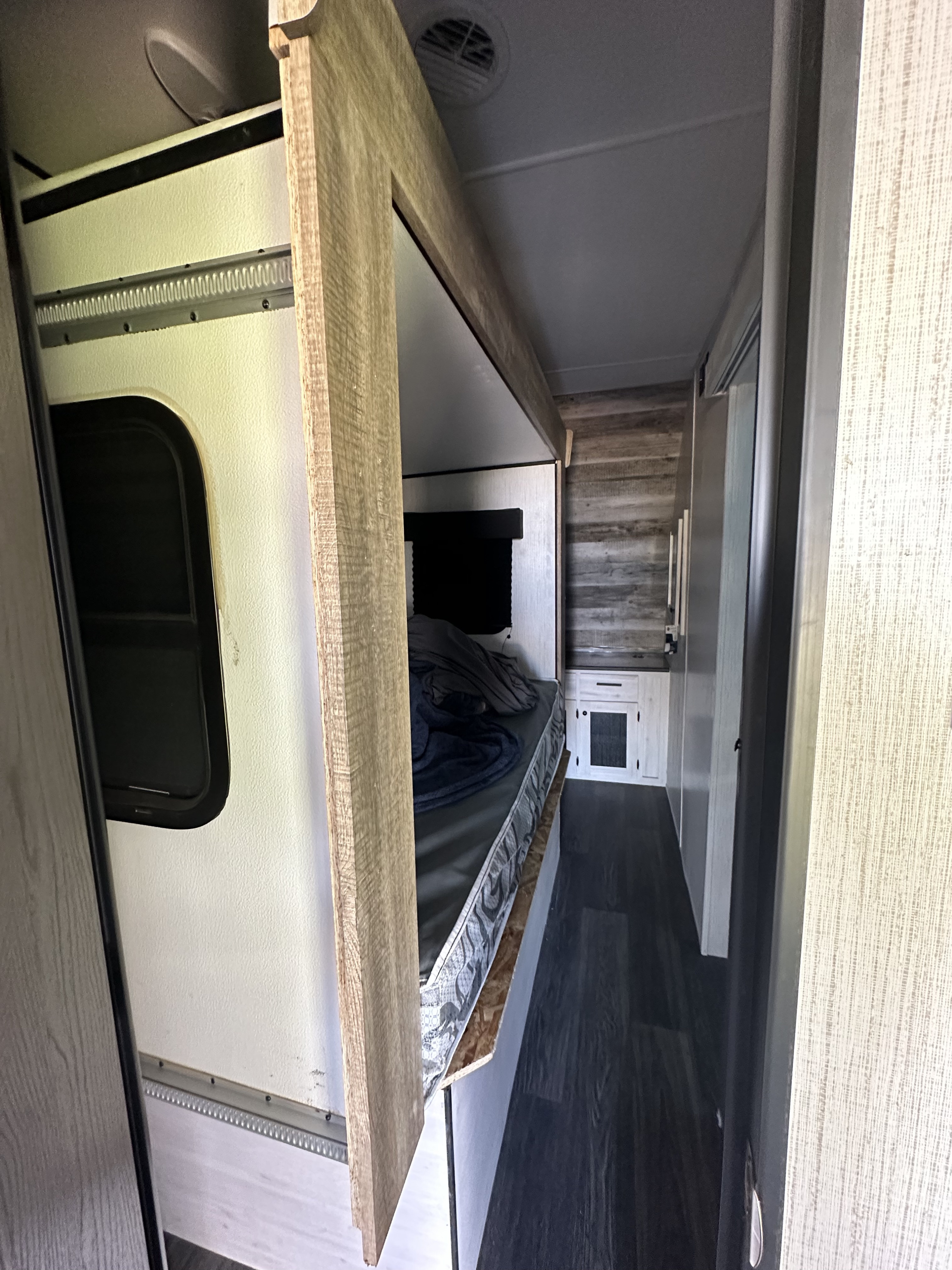 This RV rental interior shows a bunk bed with a window, a mattress with blankets, and a narrow hallway leading to a compact kitchen.. Heartland Lithium 2515S 2022