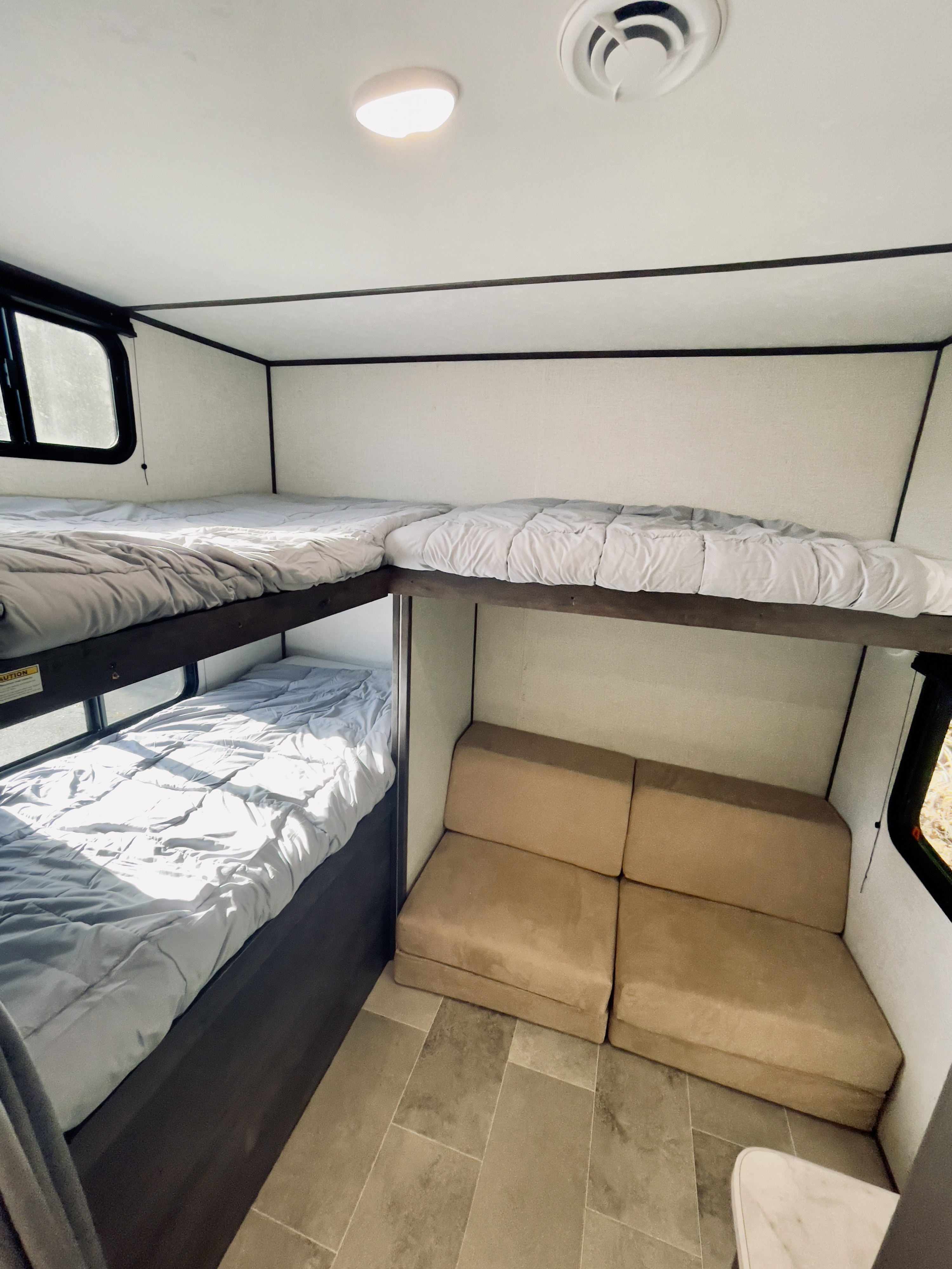 RV rental interior shows bunk beds on the left, a tan couch on the right, and a ceiling light/vent.. Dutchmen Coleman Lantern 2021