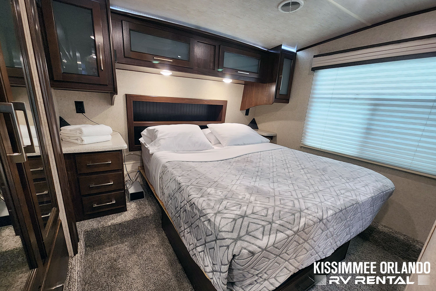 RV rental bedroom showcasing a queen bed, overhead storage, nightstands, and fresh linens. Your comfortable escape.. Heartland Cyclone 2019
