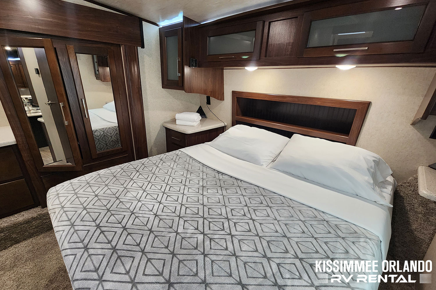 Experience comfort in this RV rental bedroom, featuring dark wood cabinetry, a cozy patterned bed, and mirrored closet doors.. Heartland Cyclone 2019