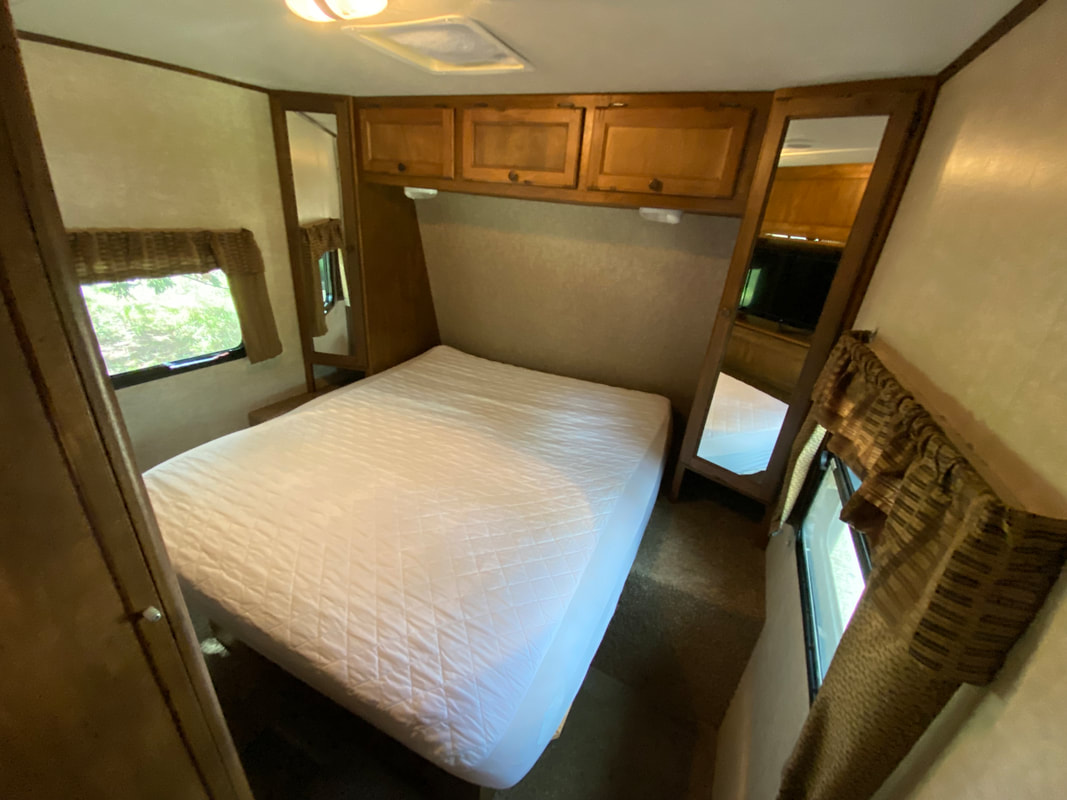 Discover the cozy bedroom of this RV rental, featuring a comfortable bed, storage cabinets, and mirrored wardrobes.. Keystone RV Sprinter 15th Anniversary 2014