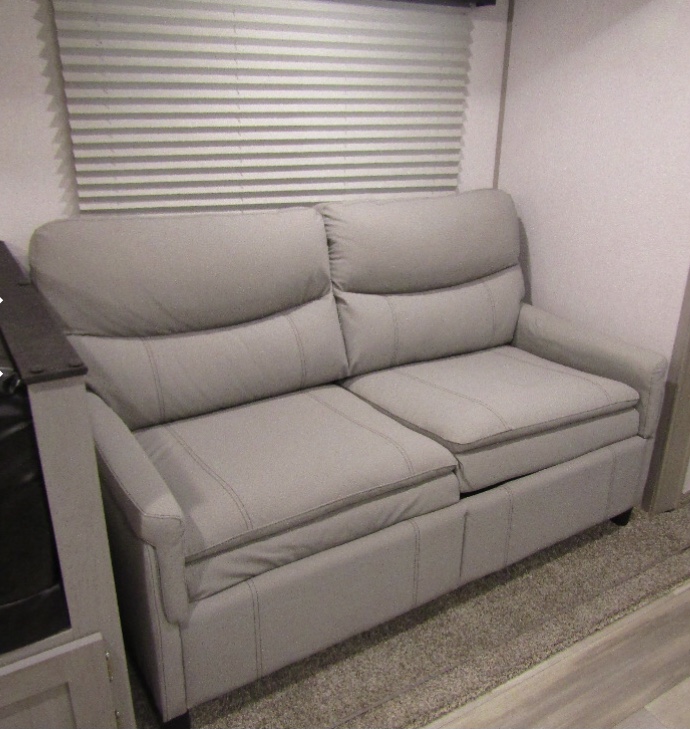 This RV rental features a comfortable gray two-seater sofa with visible stitching, set against window blinds and wood-look flooring.. Forest River Tracer 2021