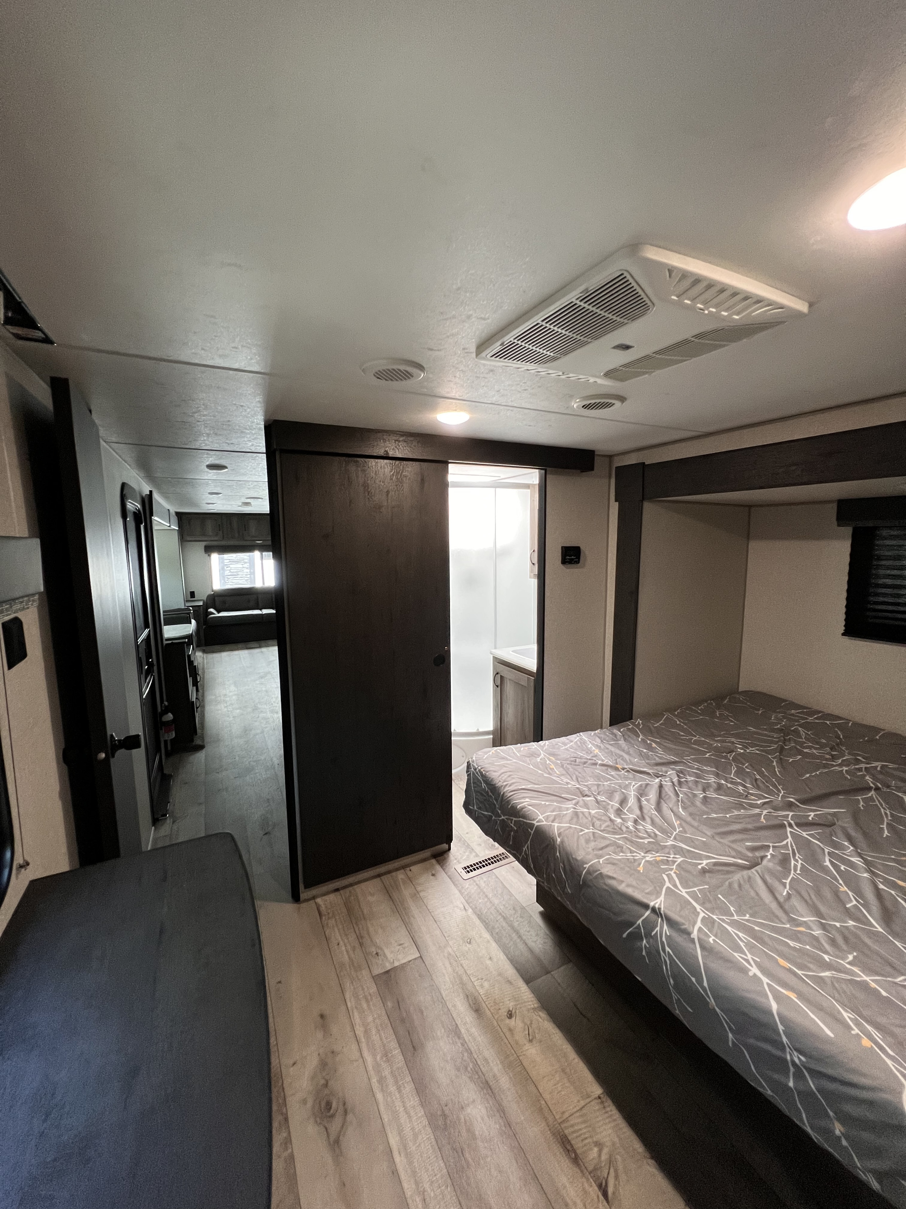 Modern RV rental interior showing a cozy bedroom, sliding door to a bathroom, and a glimpse of the living area.. KZ Sportsmen LE 303KBLE 2021