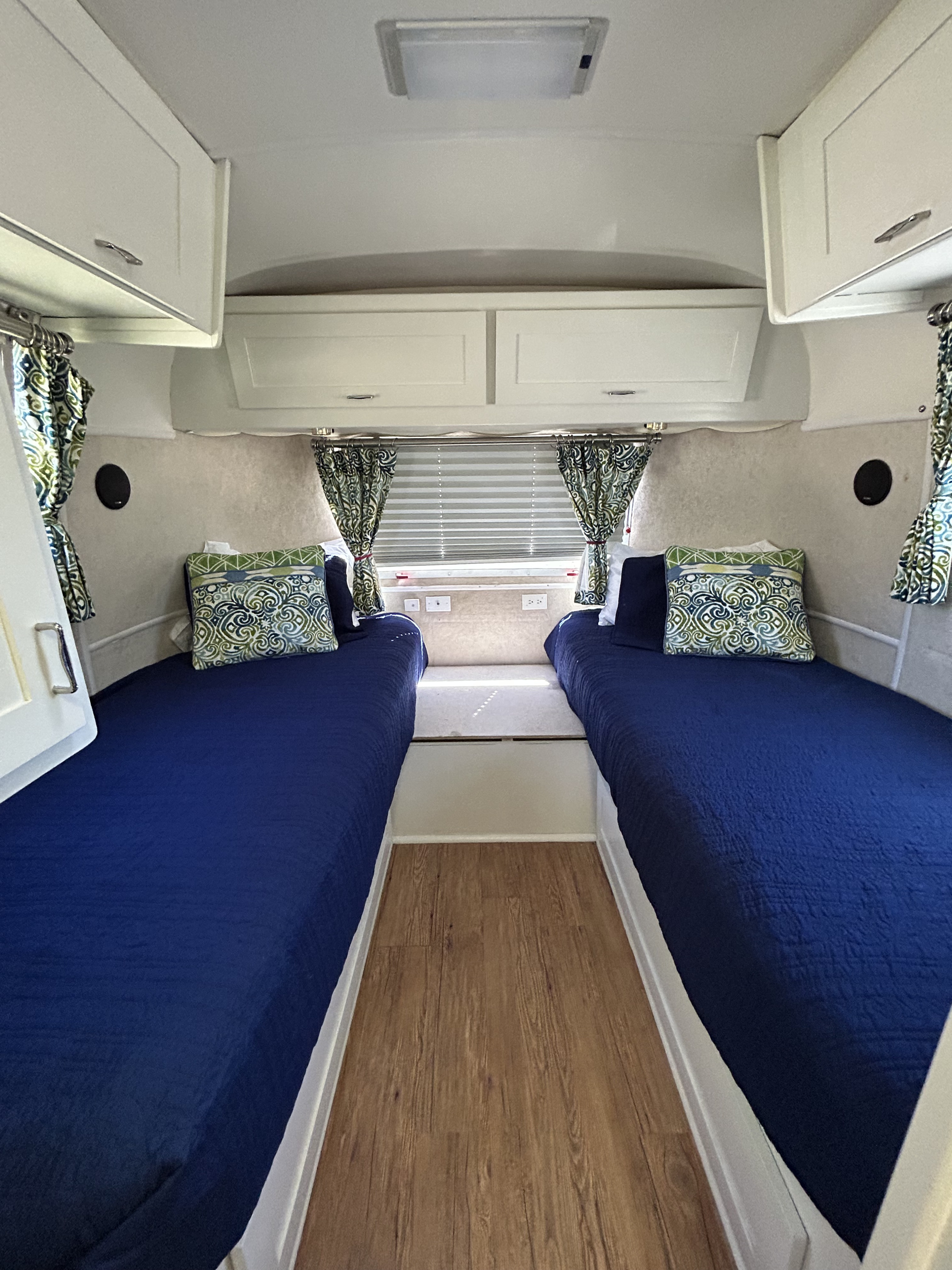 Compact RV rental bedroom interior with two twin beds featuring dark blue bedding, overhead cabinets, and patterned curtains.. Airstream Excella 2000