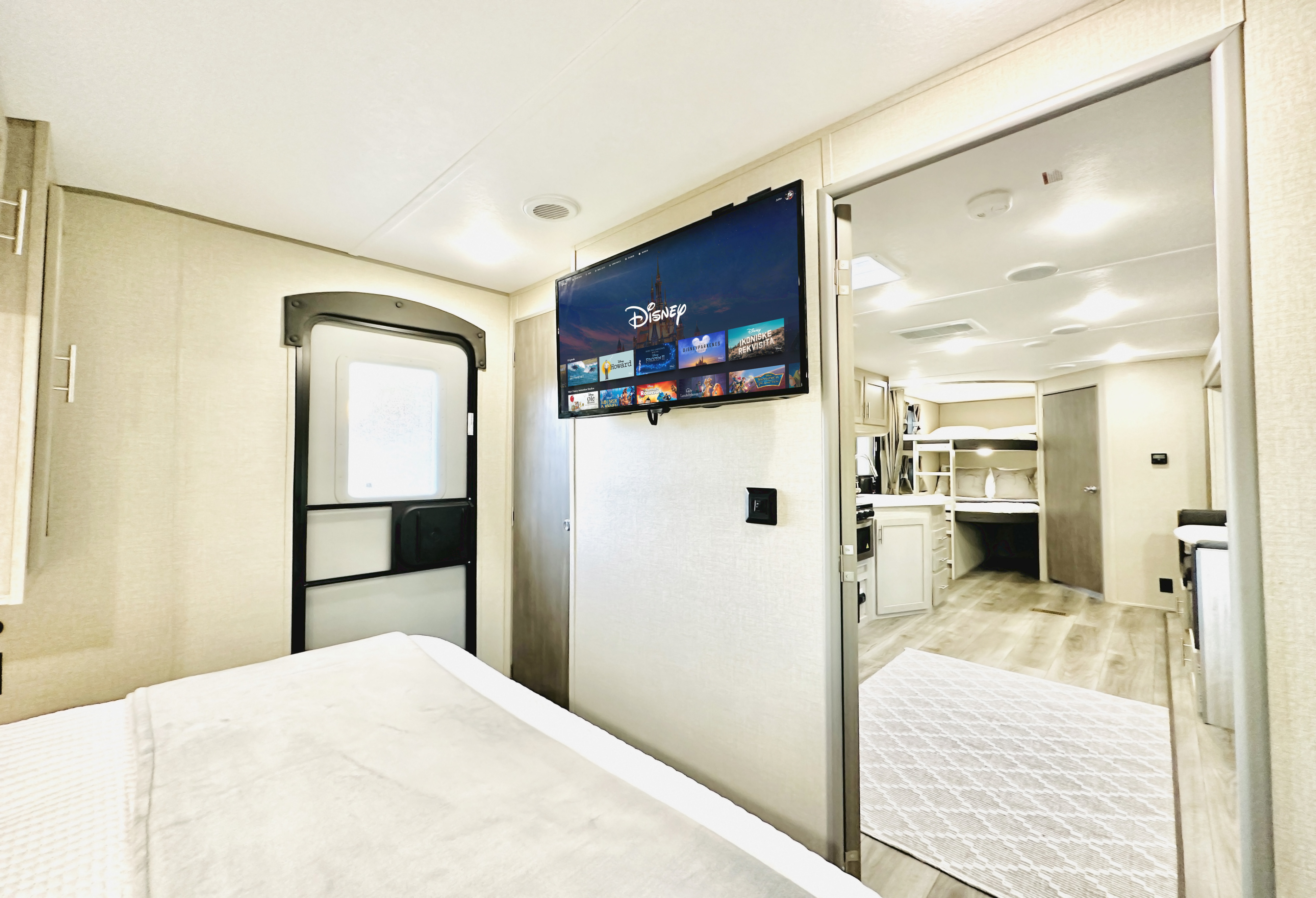 Spacious RV rental interior featuring a cozy bedroom, TV with Disney+, and an open view to the living area.. Forest River Coachmen Catalina Legacy 2023