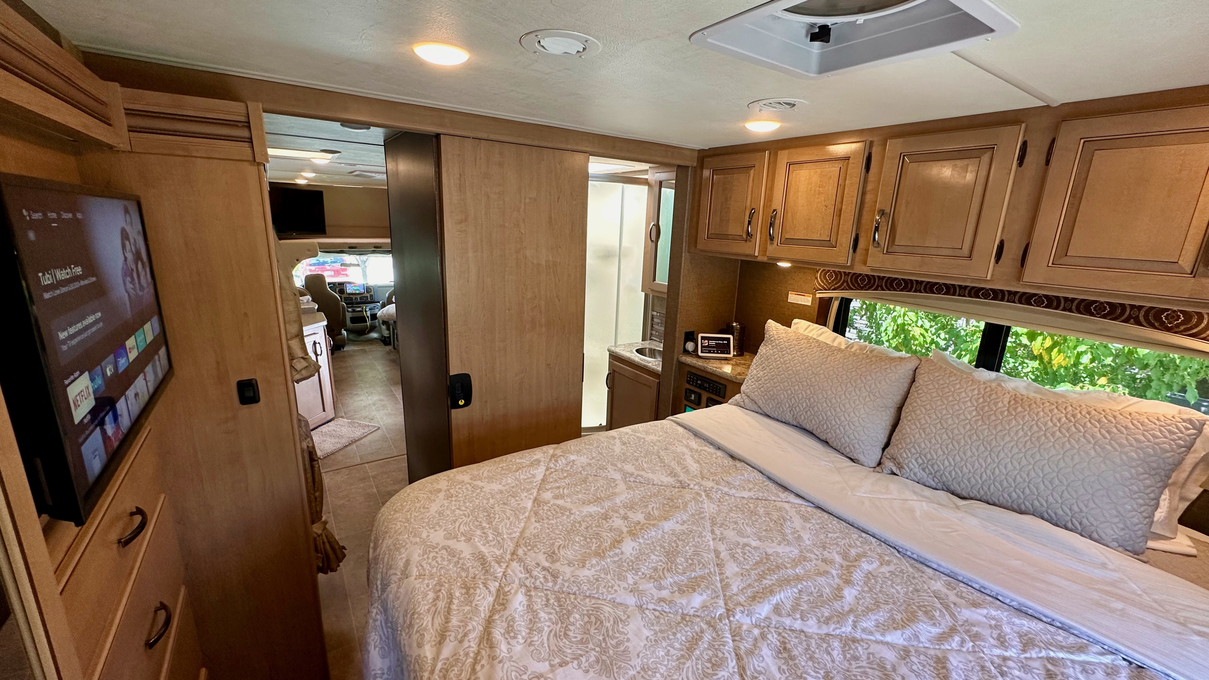 Spacious RV rental interior featuring a cozy bedroom, TV, and view into the front cabin and bathroom area.. Thor Chateau 2018