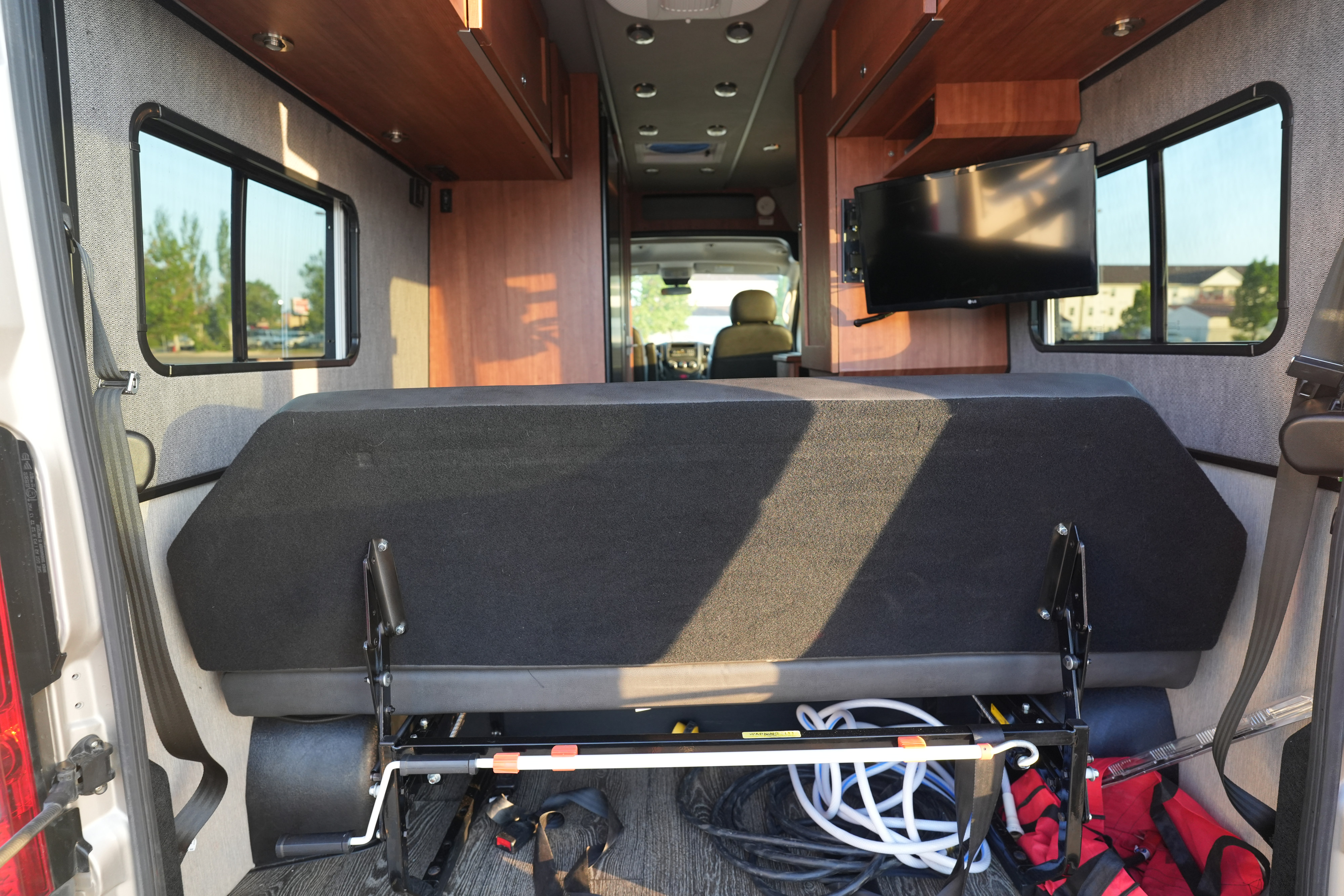 Bright RV rental interior with a convertible rear bed, under-seat storage, side windows, and a mounted TV.. Roadtrek Roadtrek Class B 2018