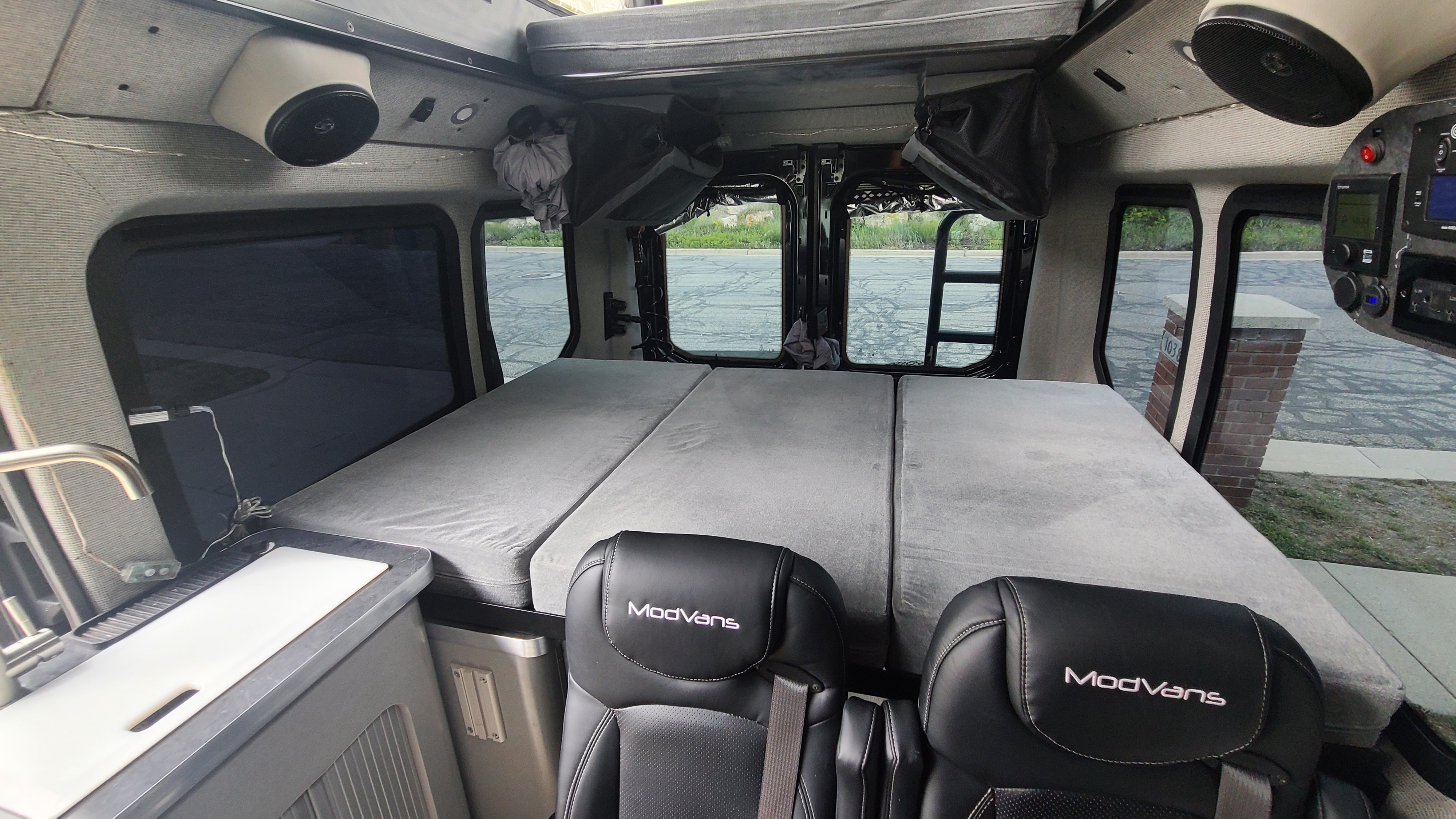 ModVans RV rental interior showing a comfortable gray bed, two front seats, and a compact kitchen counter. Ready for travel.. ModVans ModVans Class B 2021