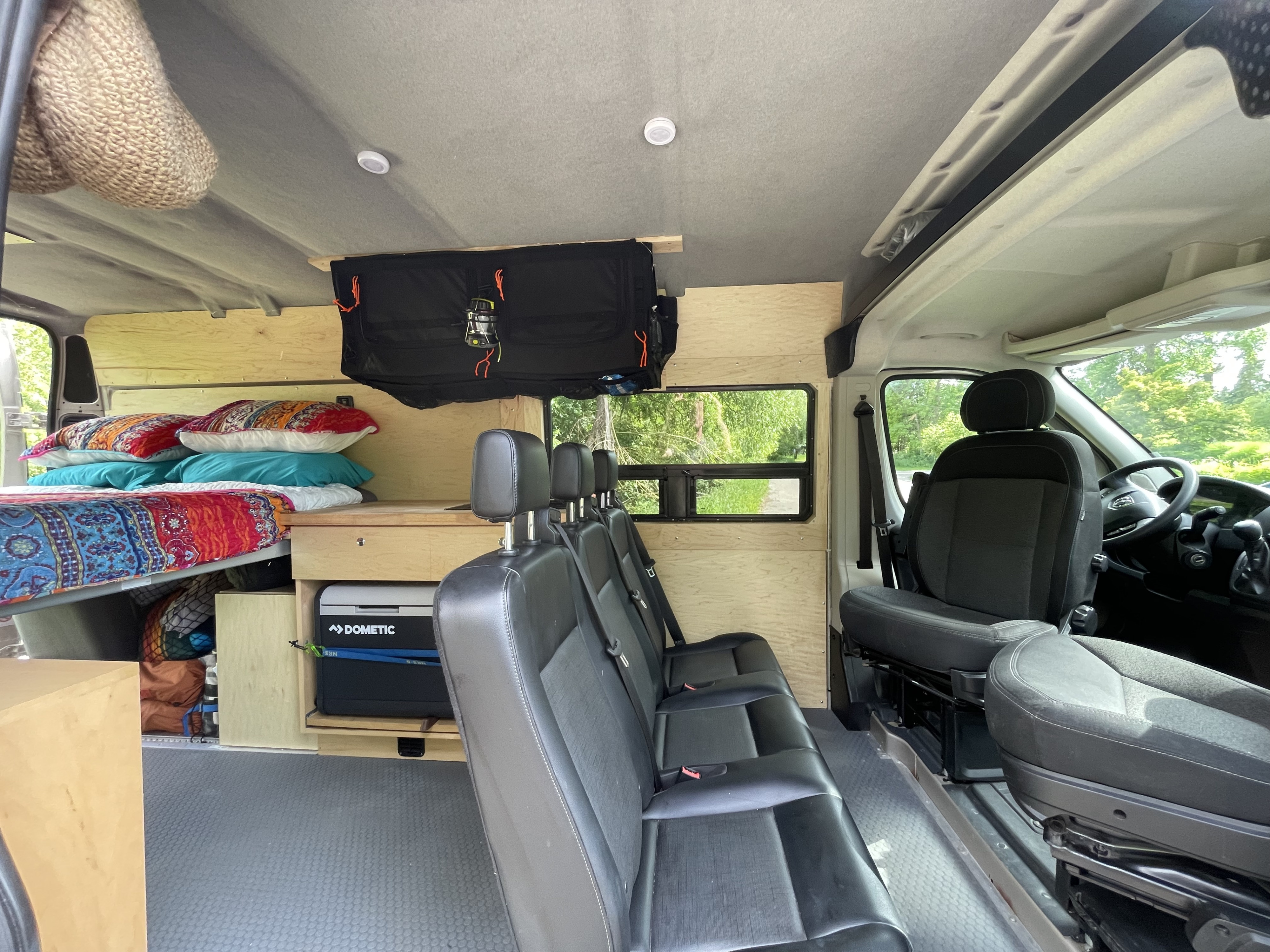 Cozy RV rental interior featuring a built-in bed with colorful pillows, multiple passenger seats, a Dometic fridge, and warm wood paneling.. Custom Camper 2016