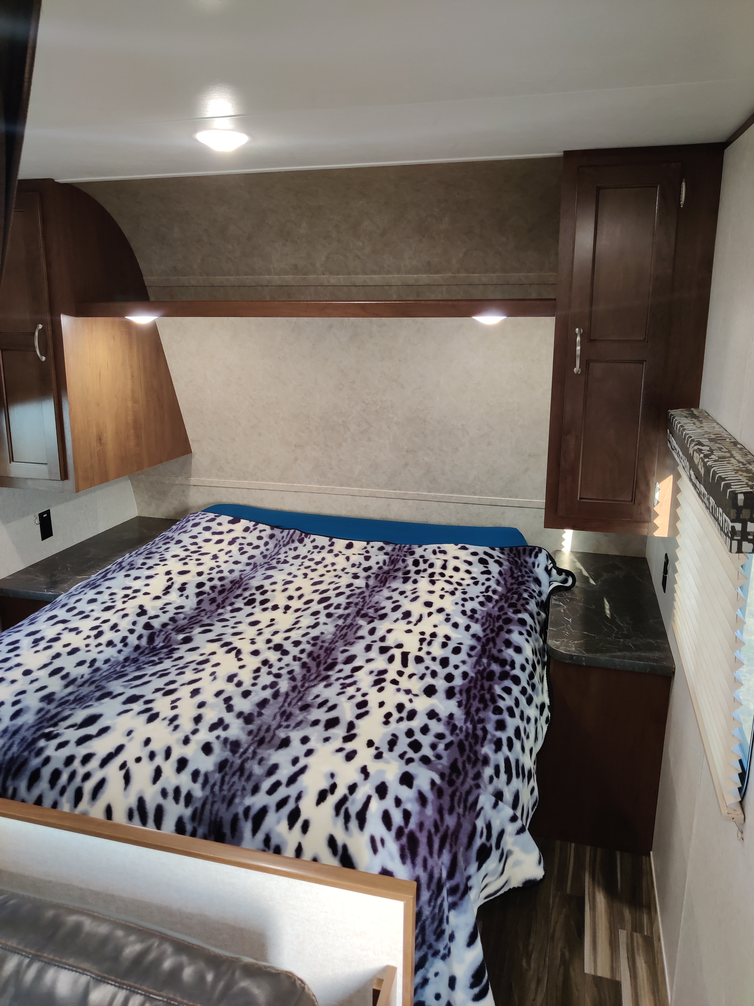 RV rental bedroom featuring a bed with a white and black spotted blanket, overhead cabinets, and built-in lighting.. Jayco Jay Flight 2017