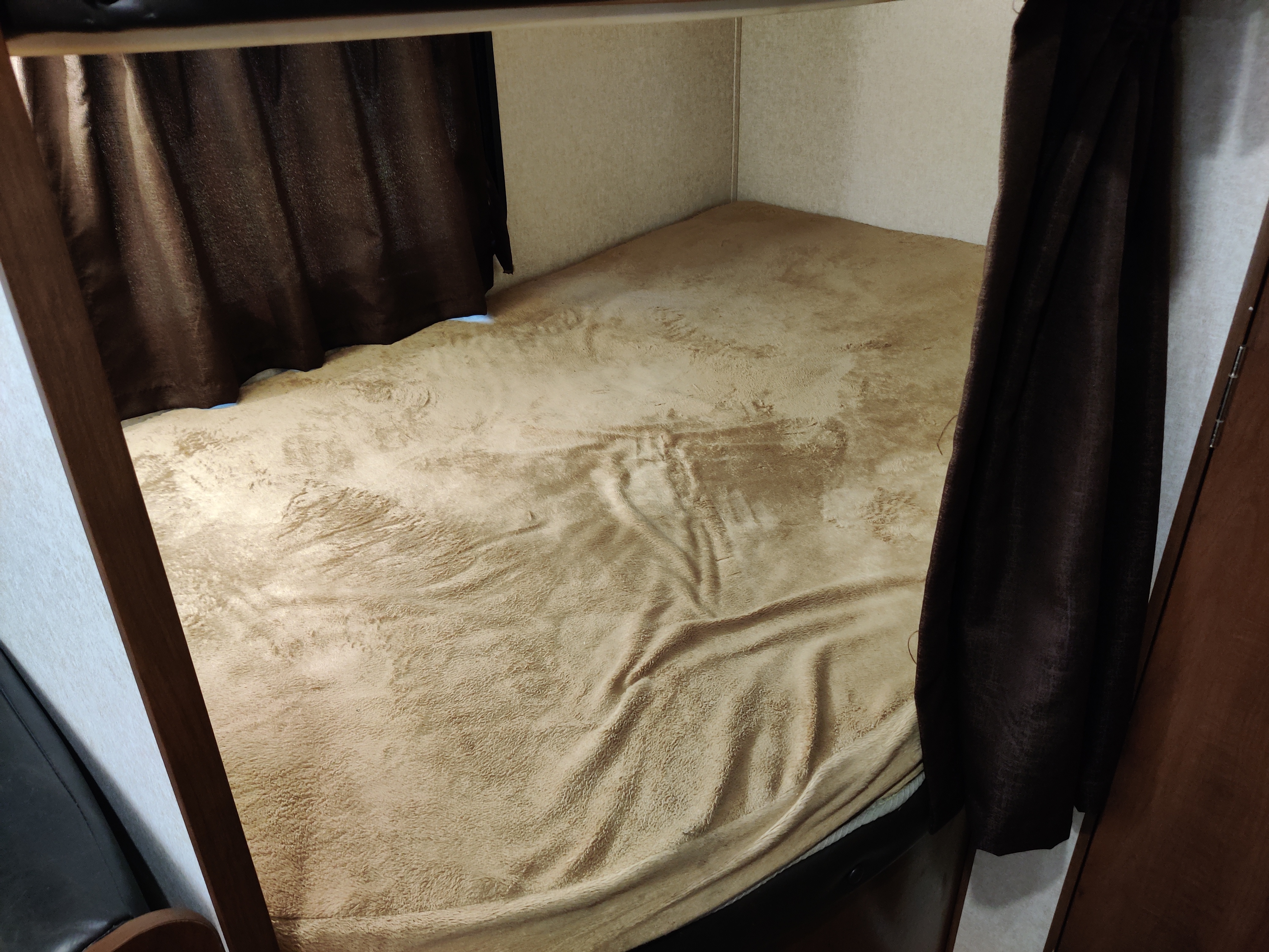An RV rental's cozy bunk bed, seen from above, with a soft beige blanket and dark privacy curtains on both sides.. Jayco Jay Flight 2017