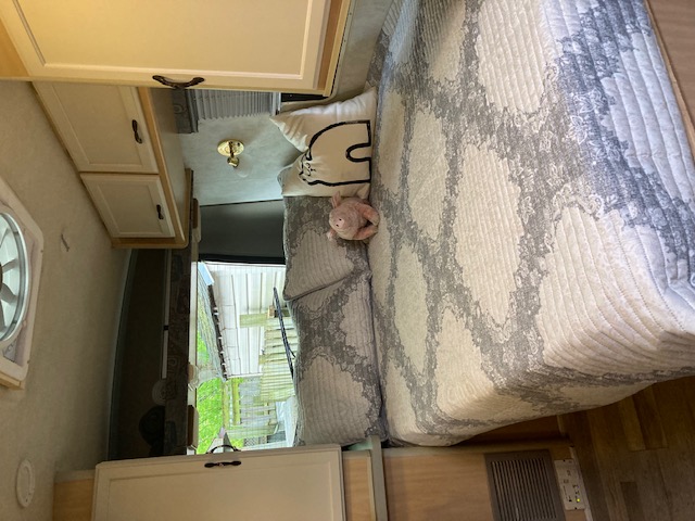 Explore this cozy RV rental bedroom, featuring a patterned bed, cat pillow, and built-in cabinets, ready for your next adventure.. Winnebago Rialta 1998
