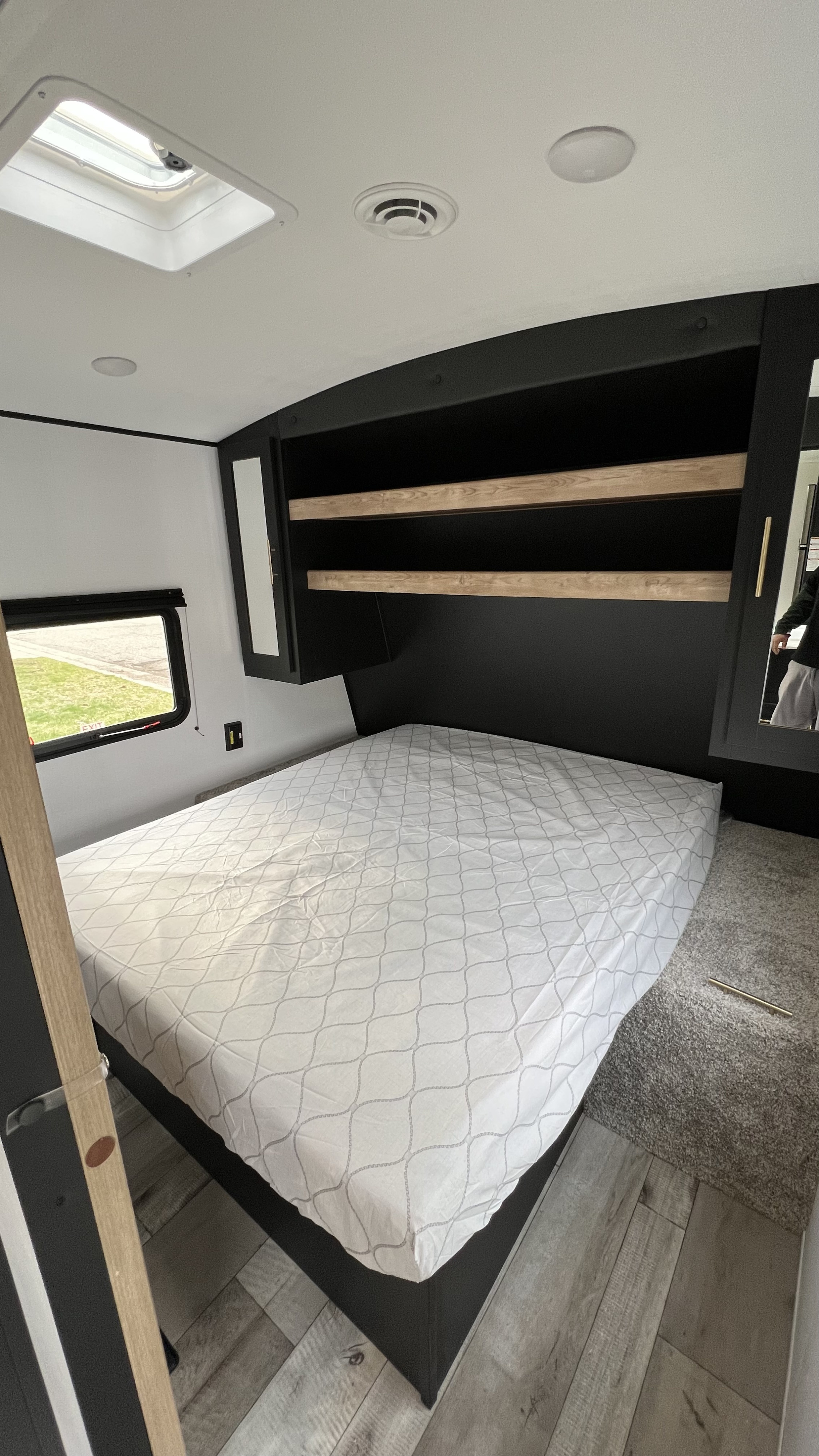 RV rental bedroom featuring a full-size bed, dark built-in storage with shelves, mirrored cabinet, and ceiling skylight.. Keystone RV Springdale 2022