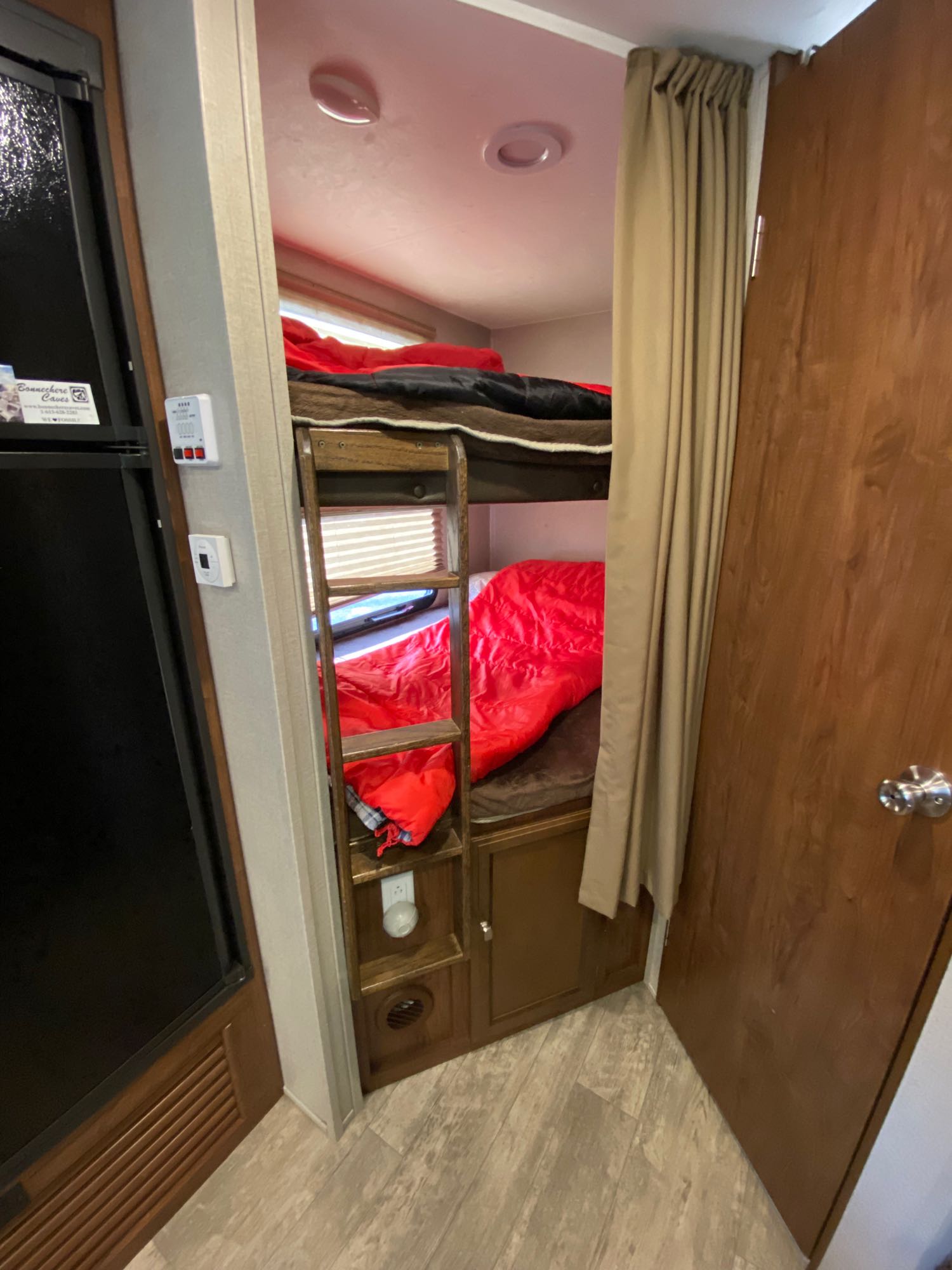 An RV rental interior showing bunk beds with a ladder, red sleeping bag, and fridge. Perfect for road trip accommodations.. Coachmen 257bhs 2017
