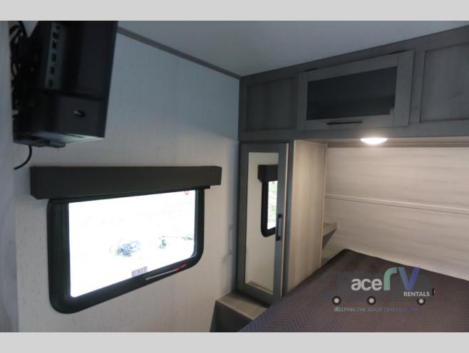 An RV rental bedroom showing a mounted TV, window with shade, overhead cabinets, and a bed for comfortable stays.. Dutchmen Kodiak Ultra Lite 2022
