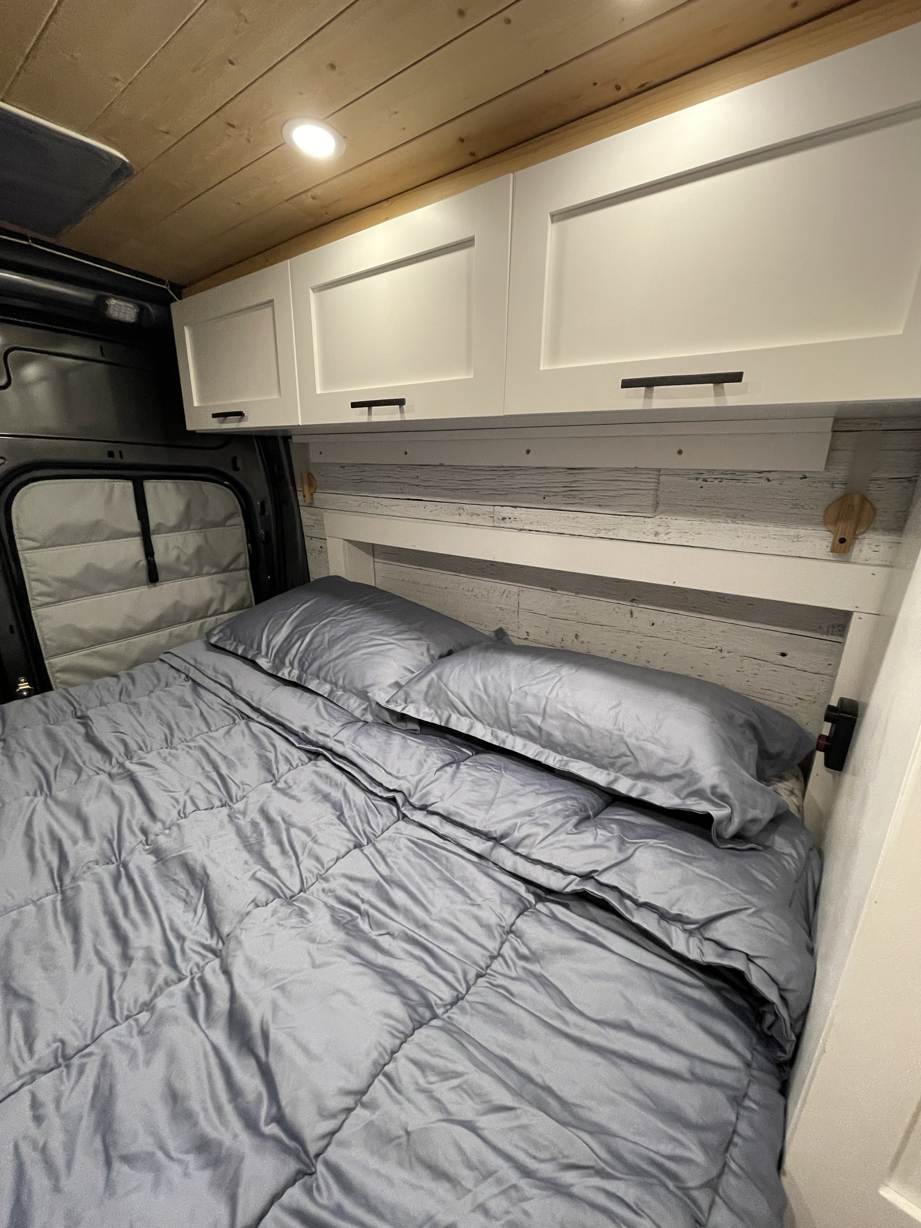 Comfortable camper van bedroom in an RV rental with a grey bed, white overhead storage, and wood plank ceiling.. Ford Transit Custom 2019