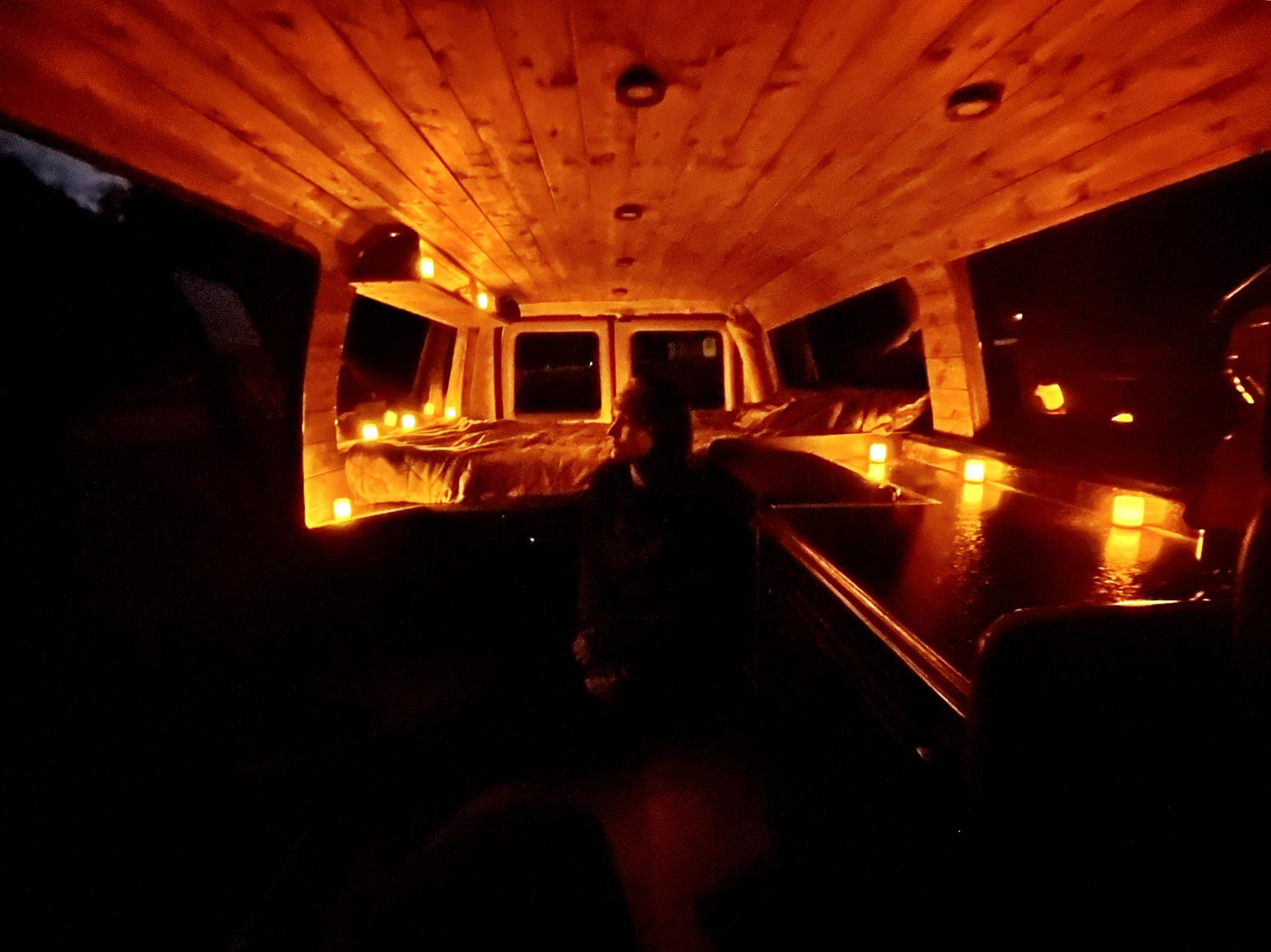 Warm glow inside this cozy RV rental van with a wooden ceiling and bed, perfect for evening comfort on your travels.. Ford Econoline 2010
