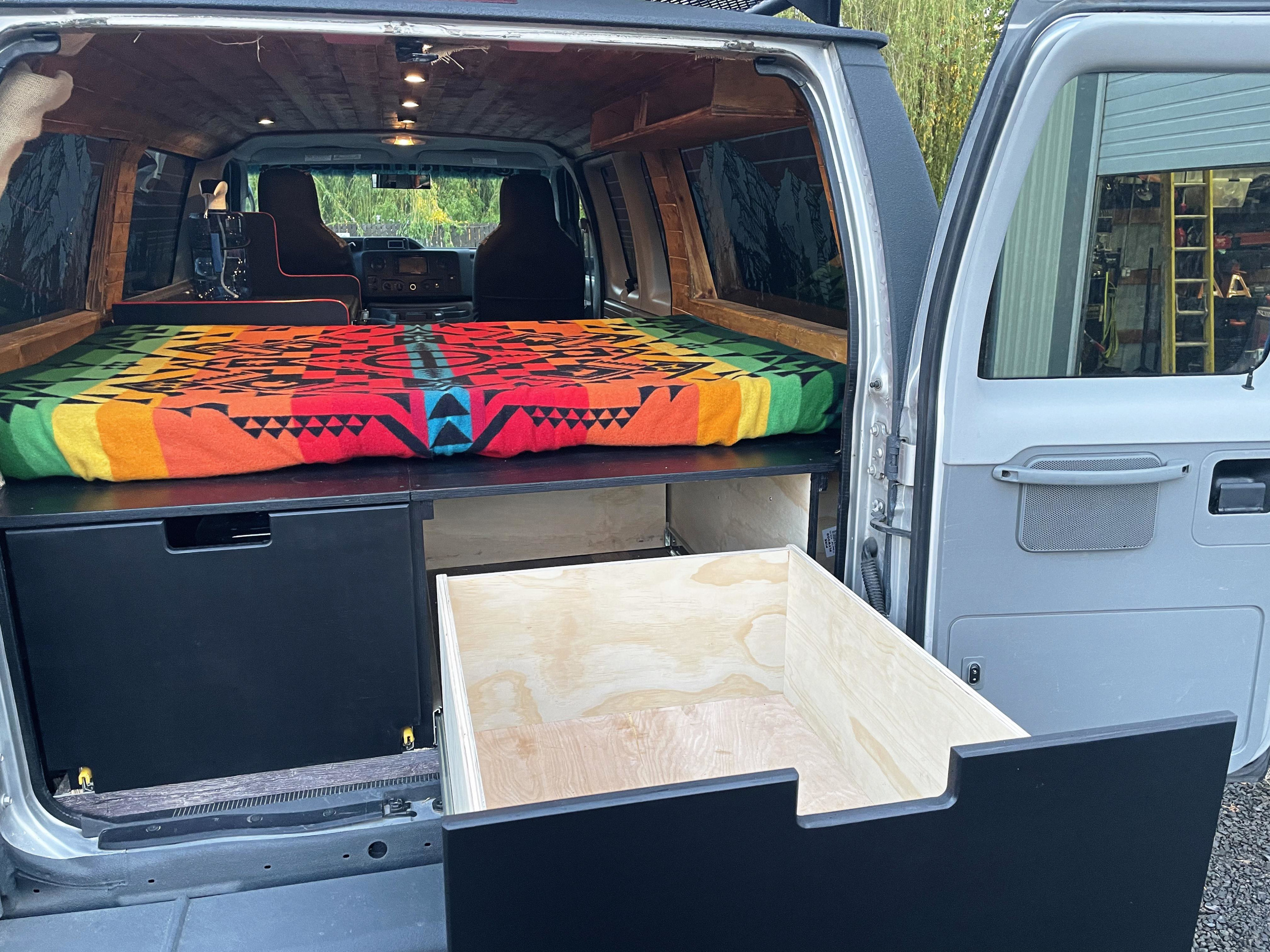 RV rental: Inside a custom camper van with a colorful bed, wooden ceiling, and a large pull-out storage drawer.. Ford Econoline 2010