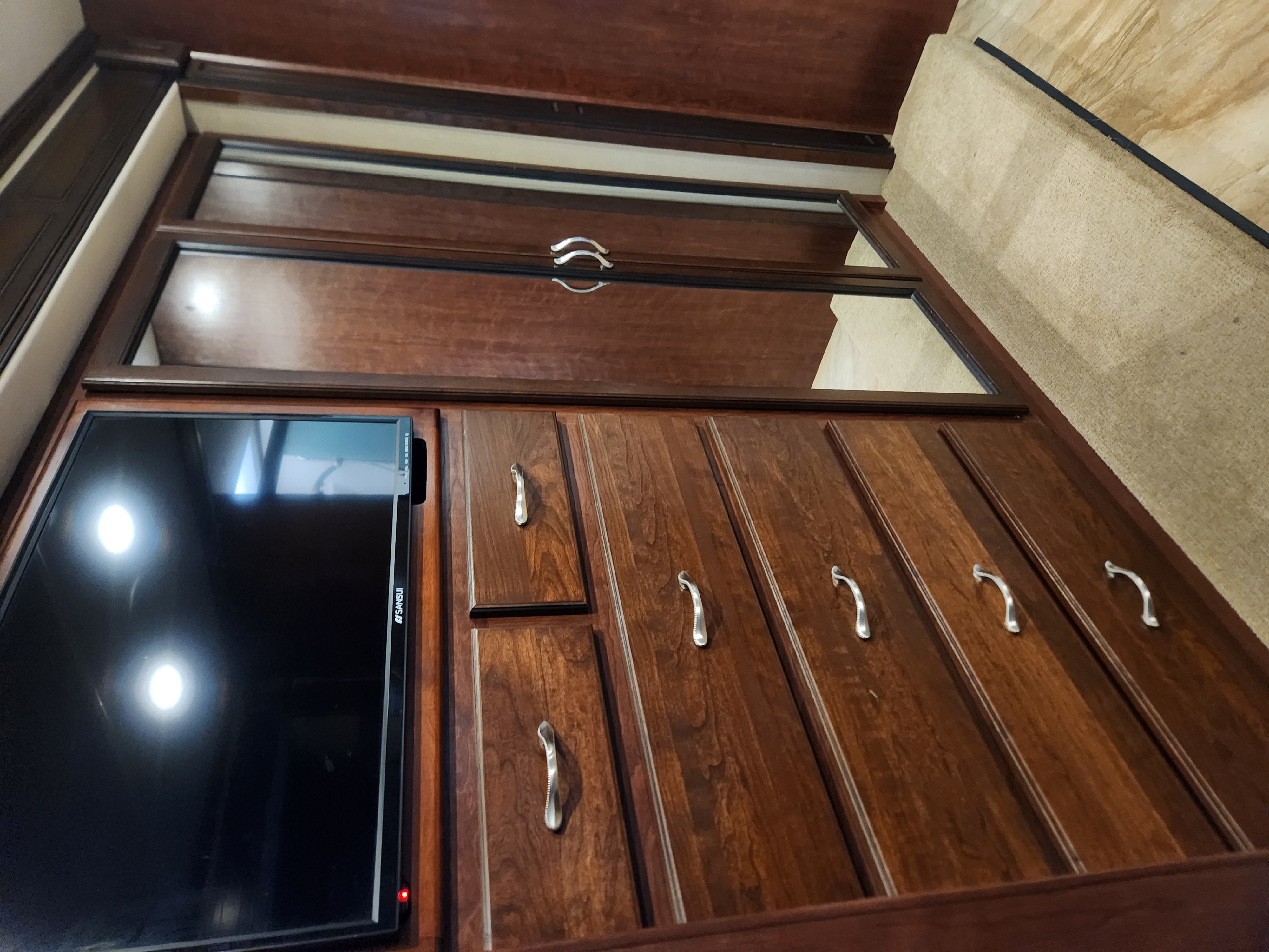 Dark brown wood cabinetry with a built-in TV and mirrored sliding doors in an RV rental bedroom, providing storage.. Fleetwood Bounder 36H 2017