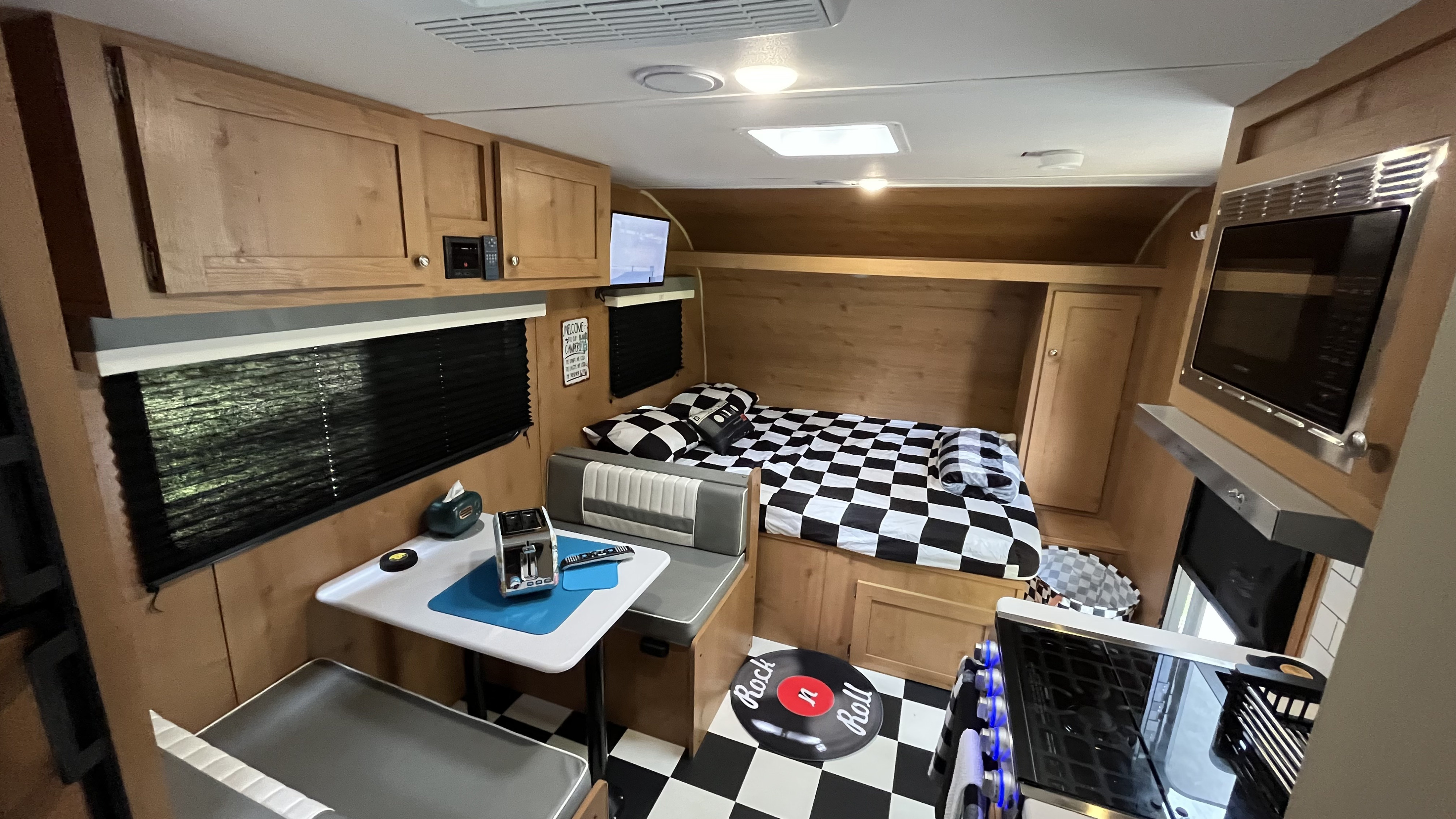 Retro-themed RV rental interior featuring a dinette, bed, and kitchen. Black and white checkered decor creates a fun vibe.. Riverside RV Retro 2022