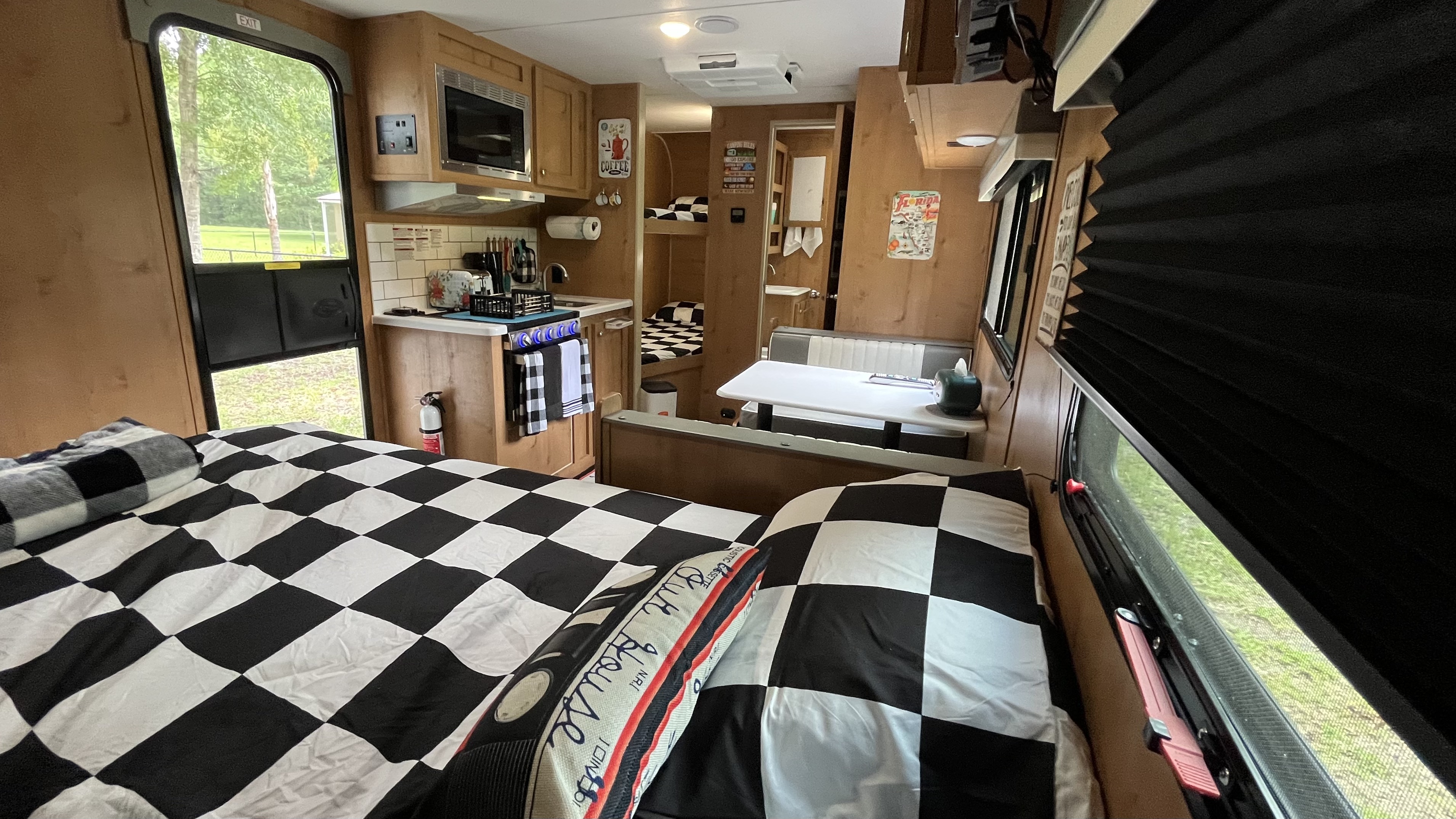 Interior of a retro-themed RV rental with black and white checkered bedding, a compact kitchen, and a dining booth, leading to bunk beds.. Riverside RV Retro 2022