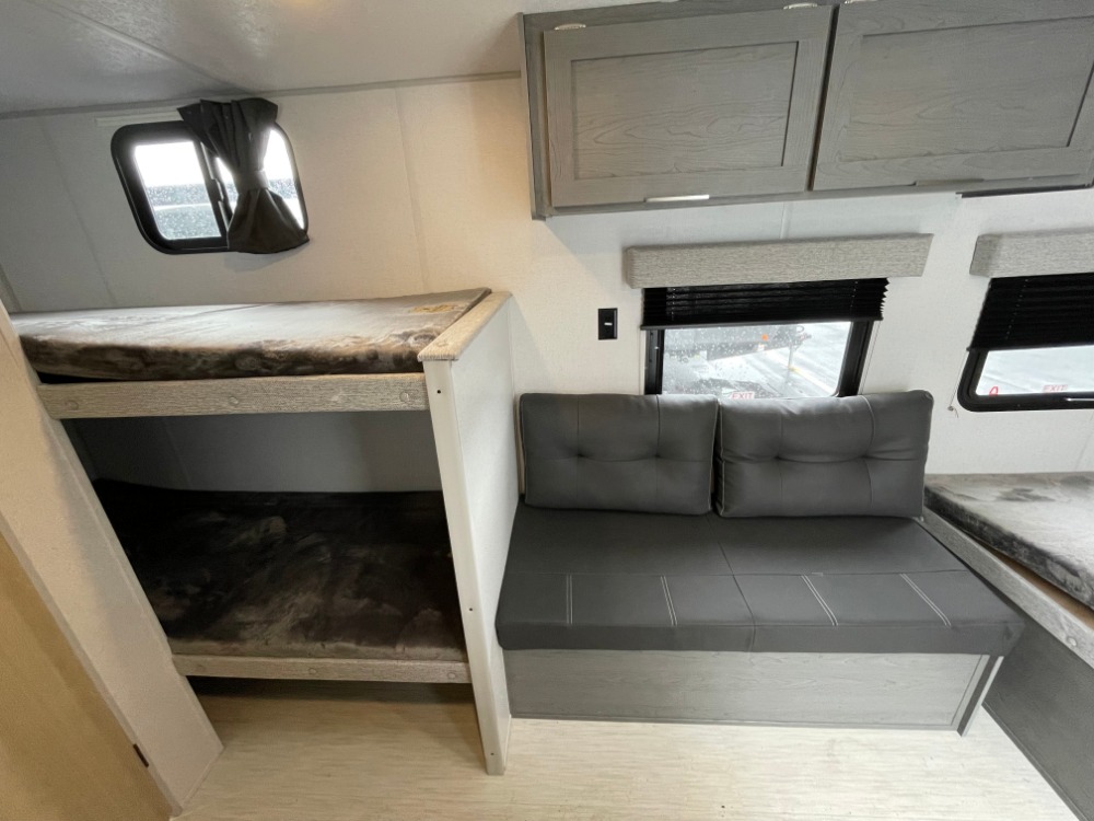 RV rental interior: bunk beds, a gray sofa with cushions, and overhead cabinets create a compact living space.. Forest River Ozark 2023