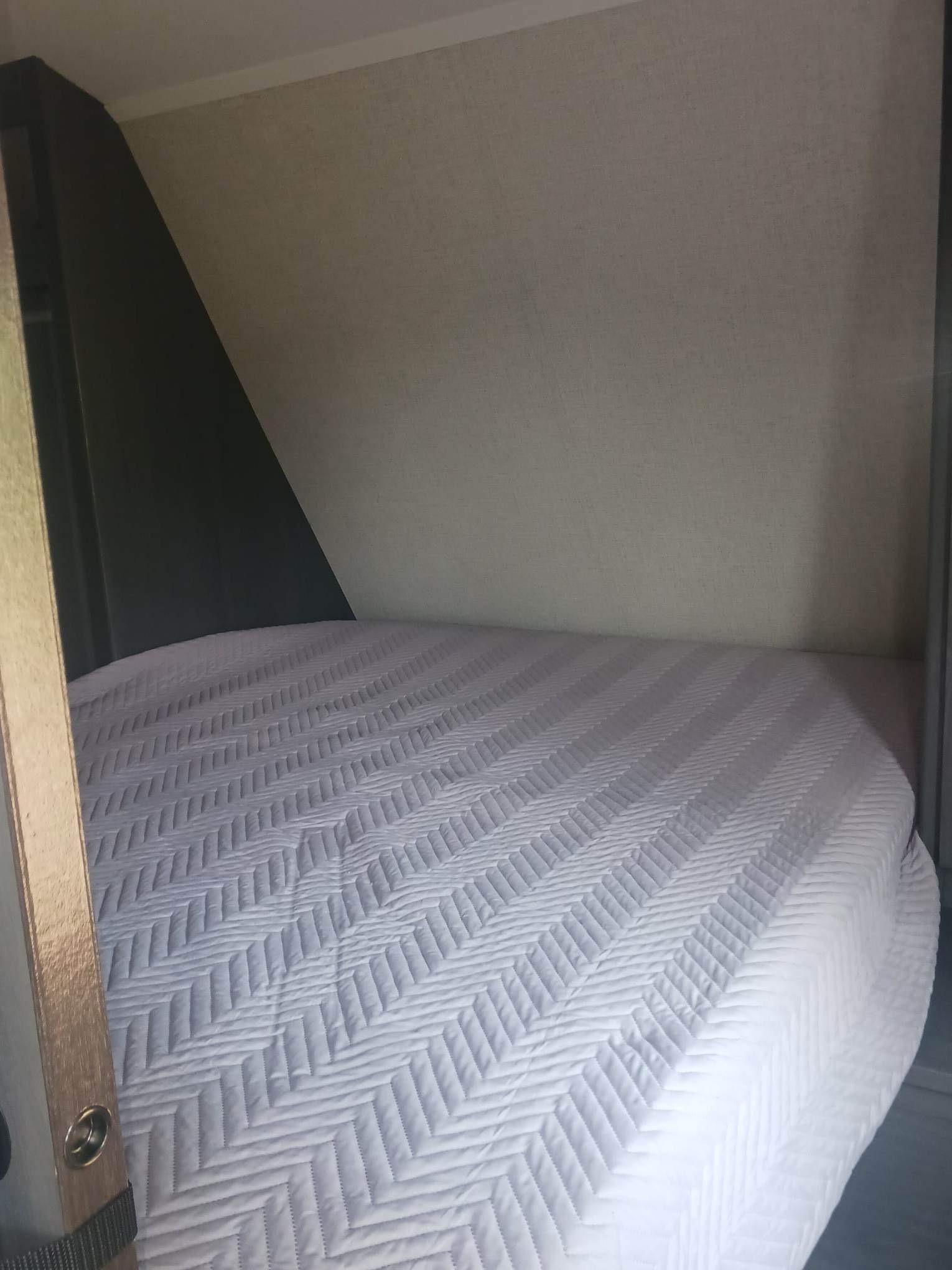 Cozy, compact bed inside an RV rental, featuring a white, chevron-quilted mattress cover and built-in storage.. Aspen Trail LE 2022