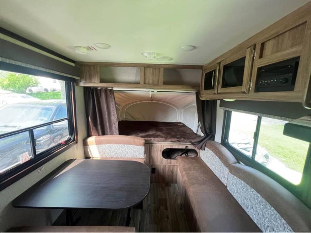 Explore this inviting RV rental interior: a comfortable dinette with patterned seating, overhead cabinets, and a cozy pop-out bed.. Jayco Jay Feather 2018