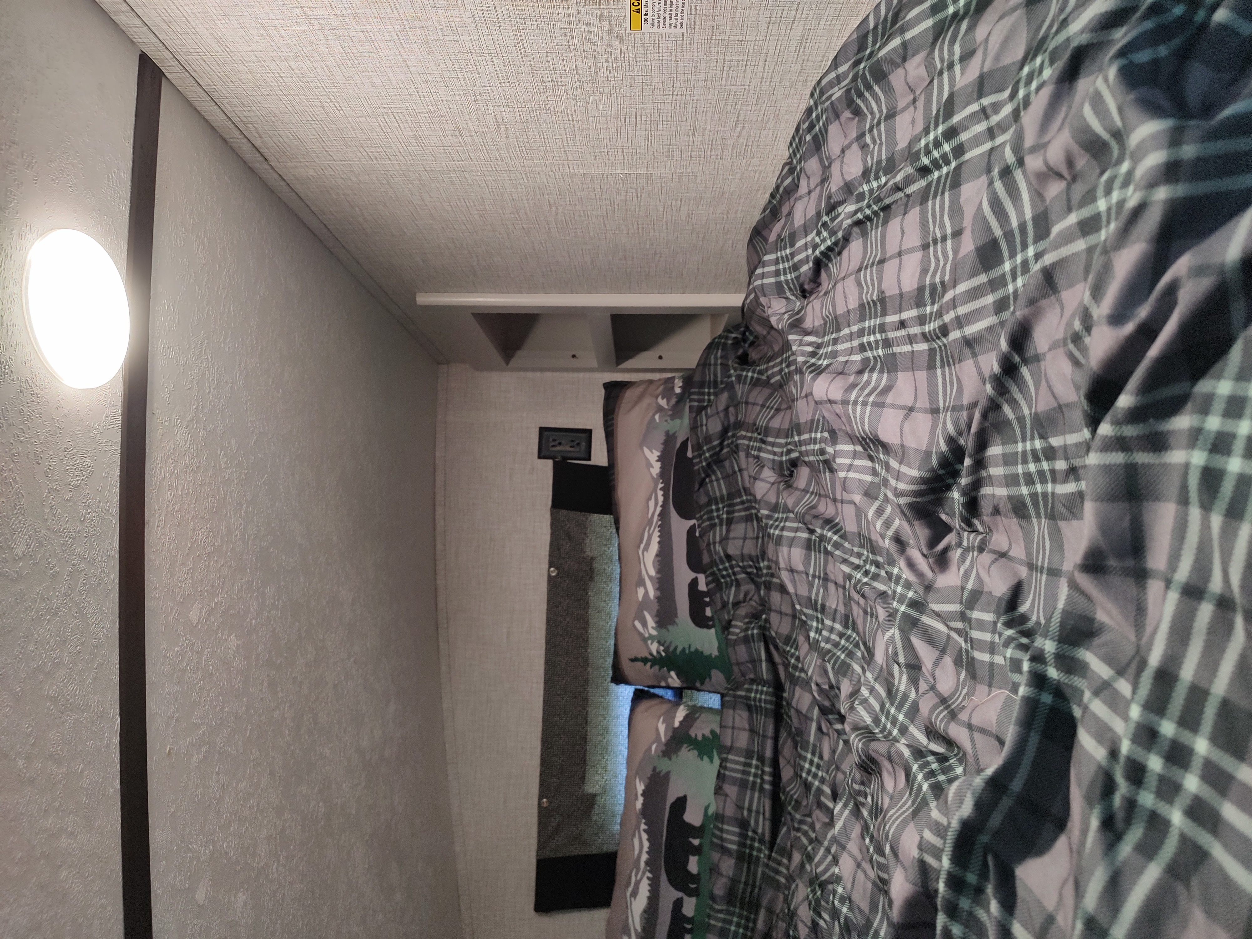 RV rental bedroom: plaid bedding, bear pillows, and an overhead bunk with a safety warning label.. Keystone RV Bullet Ultra Lite 2021