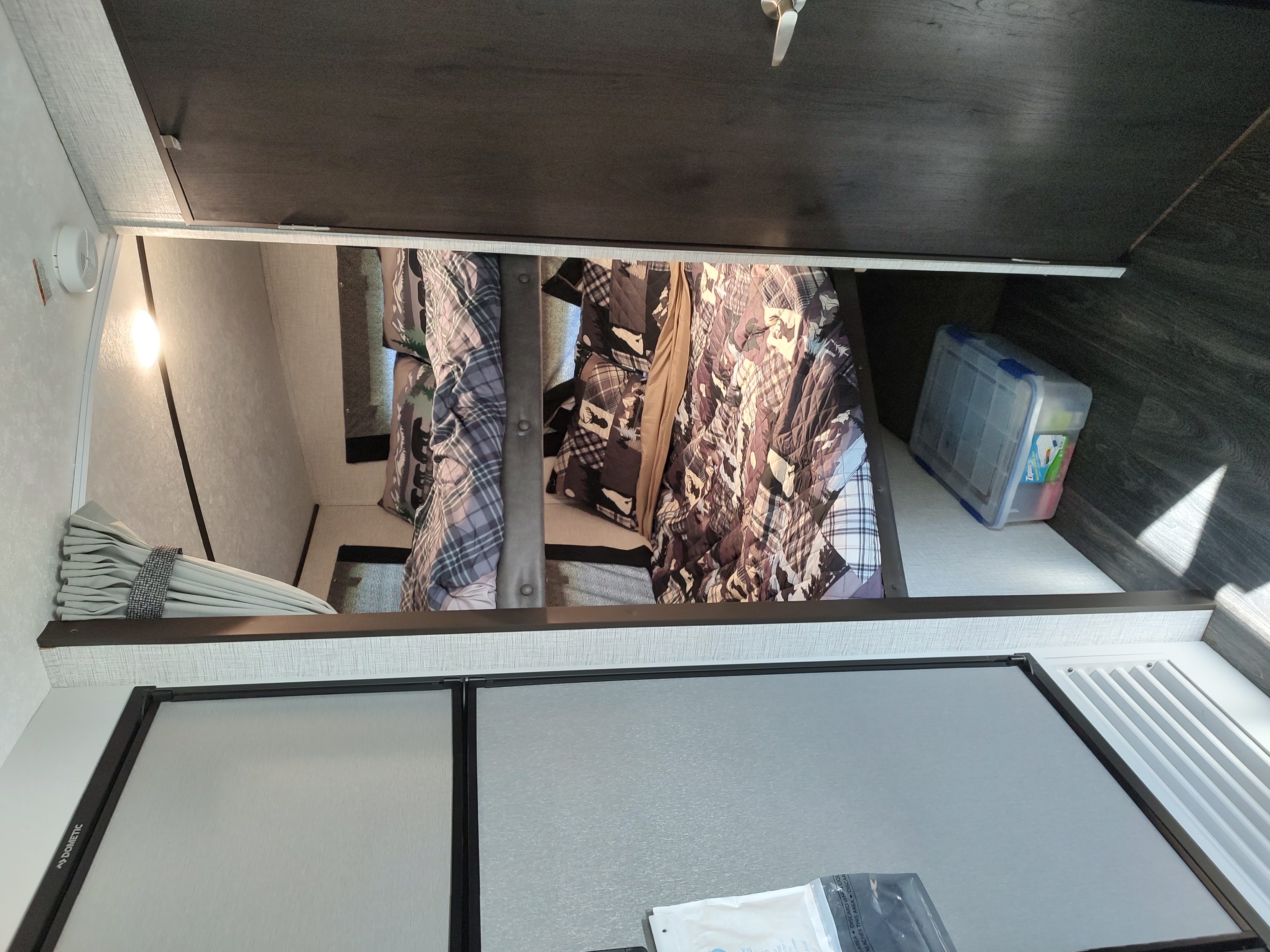 RV rental bunk beds. Upper and lower bunks with bedding, a light, and a Dometic refrigerator shown in this compact interior.. Keystone RV Bullet Ultra Lite 2021