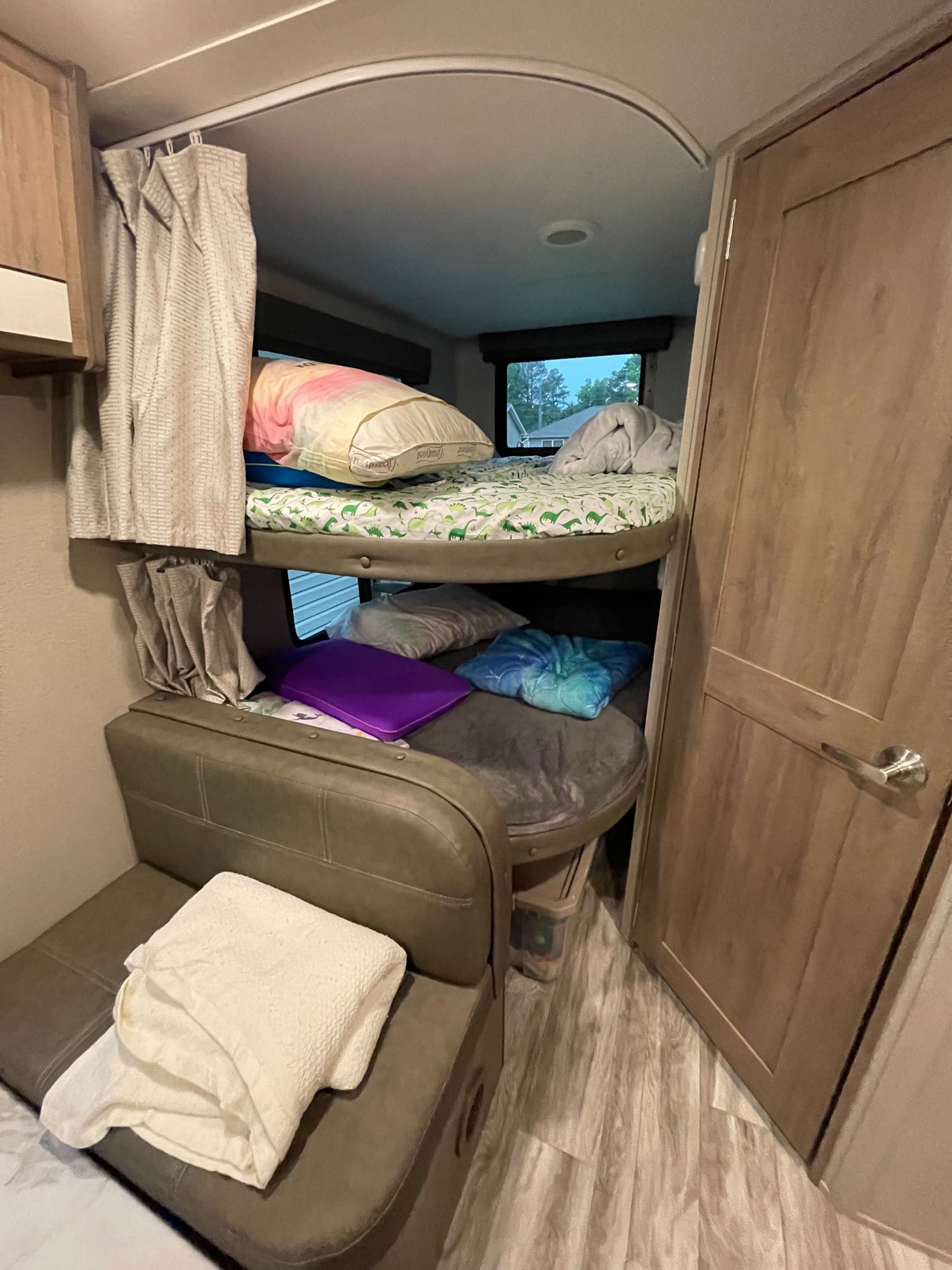 RV rental interior. Features stacked bunk beds with bedding, privacy curtains, and a small sofa, optimized for compact living.. Grand Design Imagine XLS 2022
