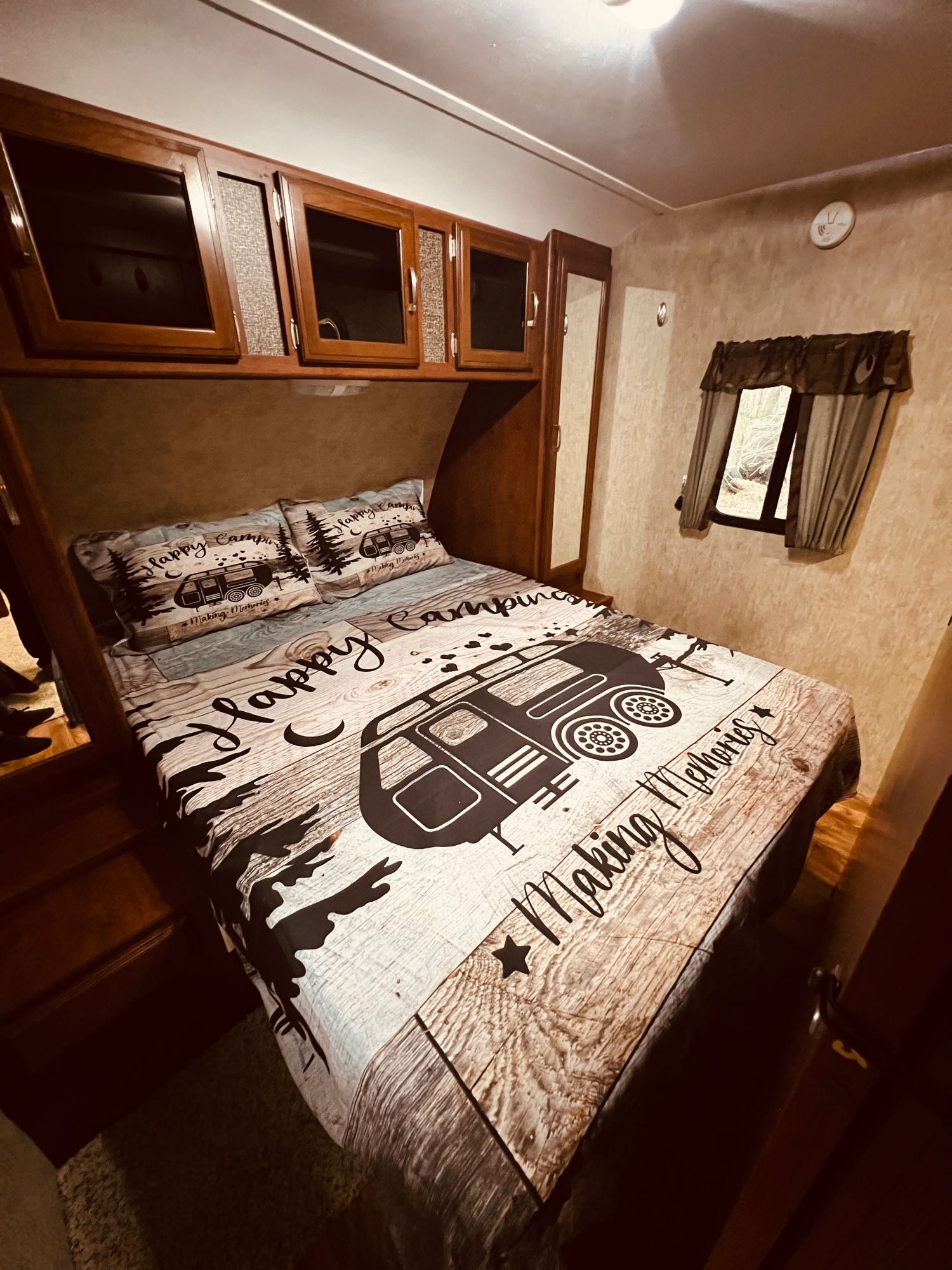 Cozy RV rental bedroom with "Happy Camping" bedding, overhead cabinets, and a window for scenic views.. Keystone RV Passport Grand Touring 2016