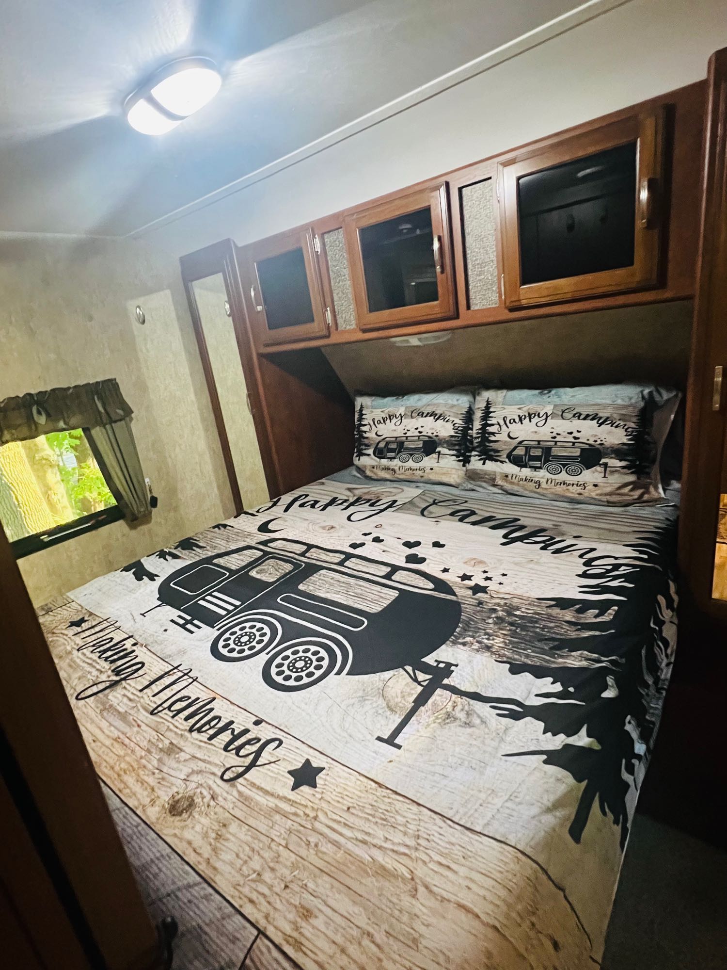 Cozy RV rental bedroom with "Happy Camping" themed bedding and overhead storage, ideal for travel trailer adventures.. Keystone RV Passport Grand Touring 2016