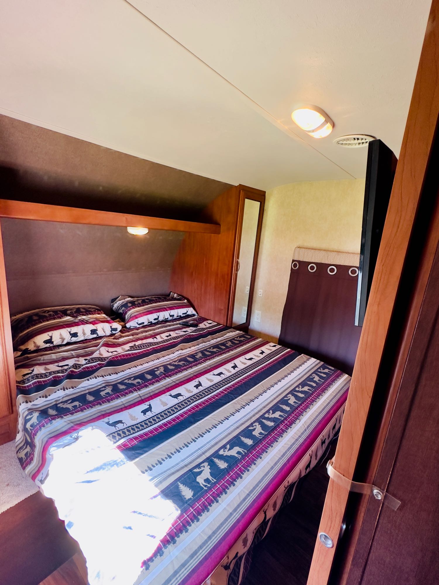 Cozy RV rental bedroom featuring a large bed with striped deer and tree bedding, overhead lighting, and built-in storage.. Forest River Salem Cruise Lite 2015