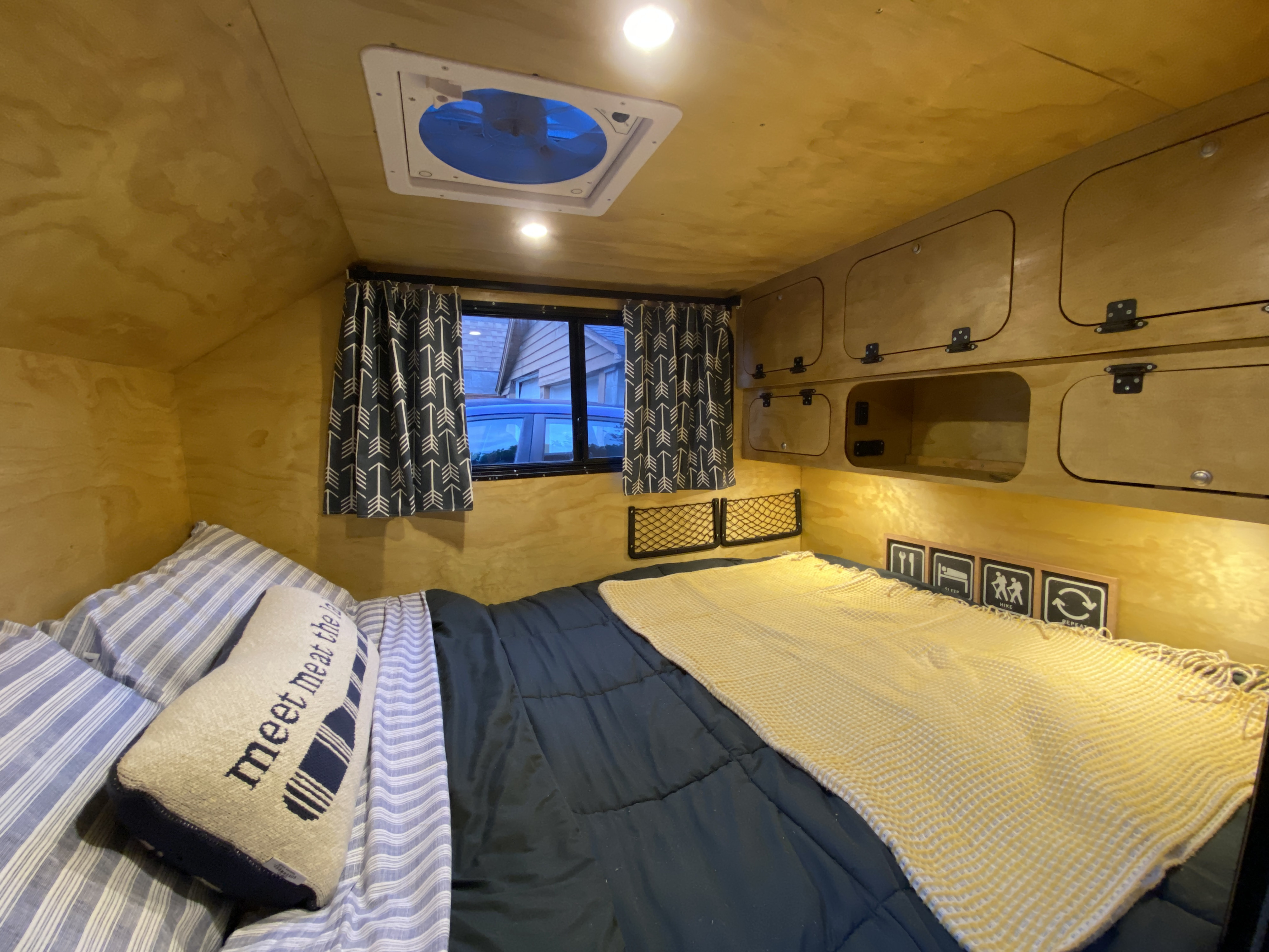 Inside a cozy RV rental: a comfy bed, wood walls, overhead storage, a window, and ceiling fan.. U-Bilt U-Bilt 2021