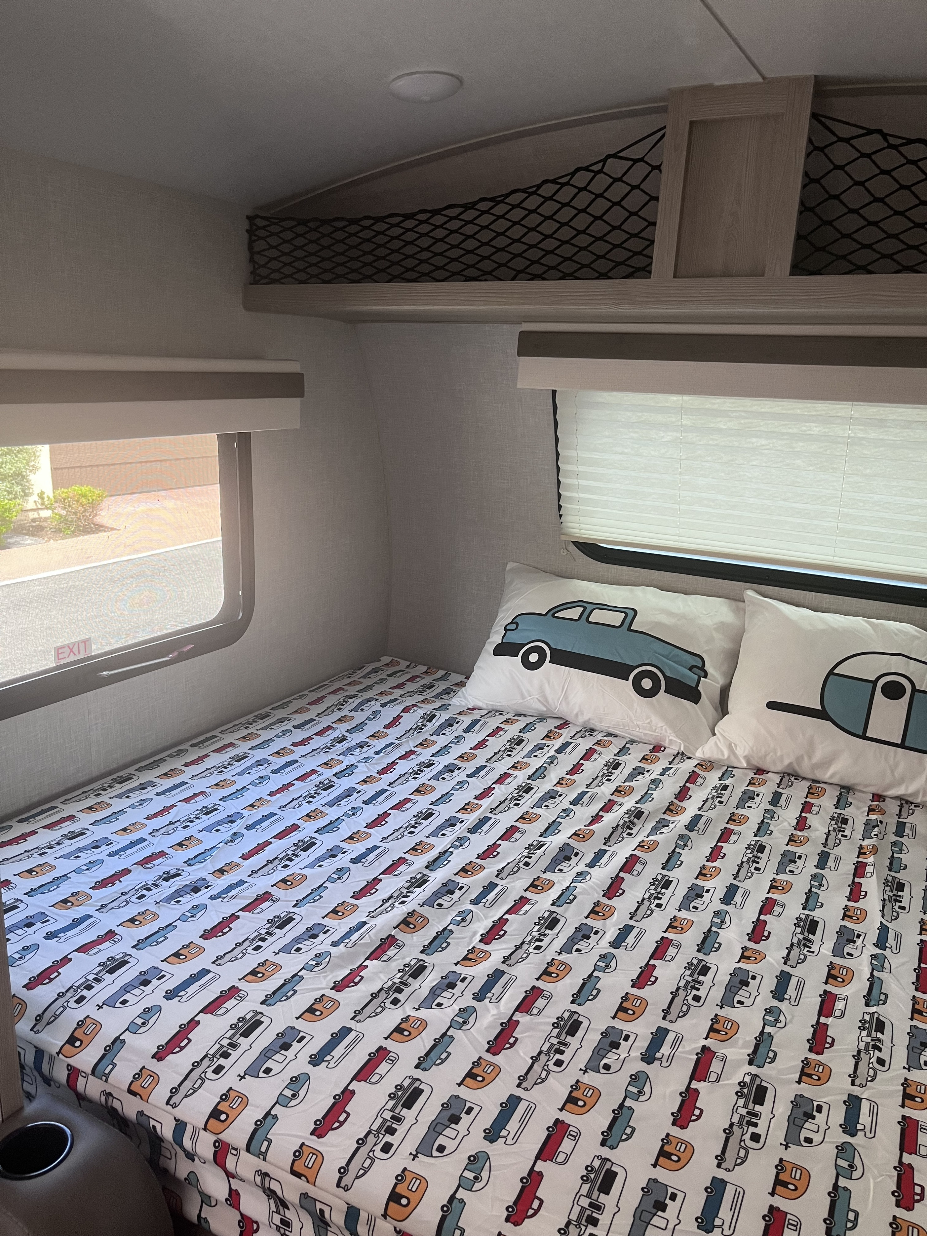 Inside an RV rental: A child's bunk bed with car and camper patterned sheets and pillows. Overhead net storage is visible.. Forest River Rockwood Geo Pro 2022