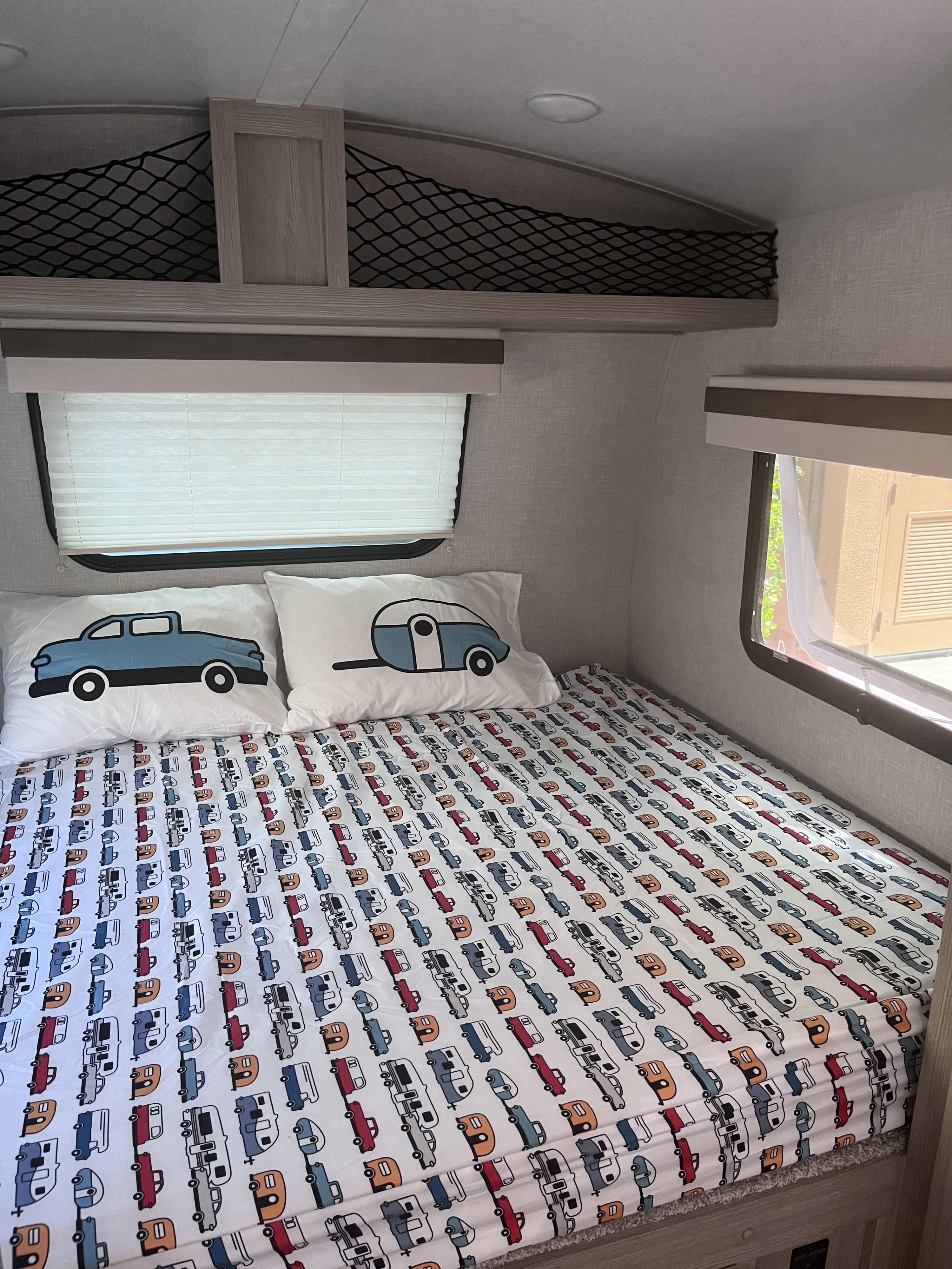 Cozy RV rental sleeping area with fun camper and car patterned bedding, pillows, overhead storage nets, and windows.. Forest River Rockwood Geo Pro 2022