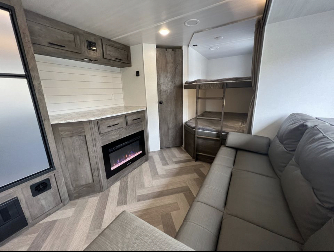 Inside this RV rental: a cozy grey sofa, built-in bunk beds, electric fireplace, and ample storage cabinetry.. Forest River Wildwood 2021