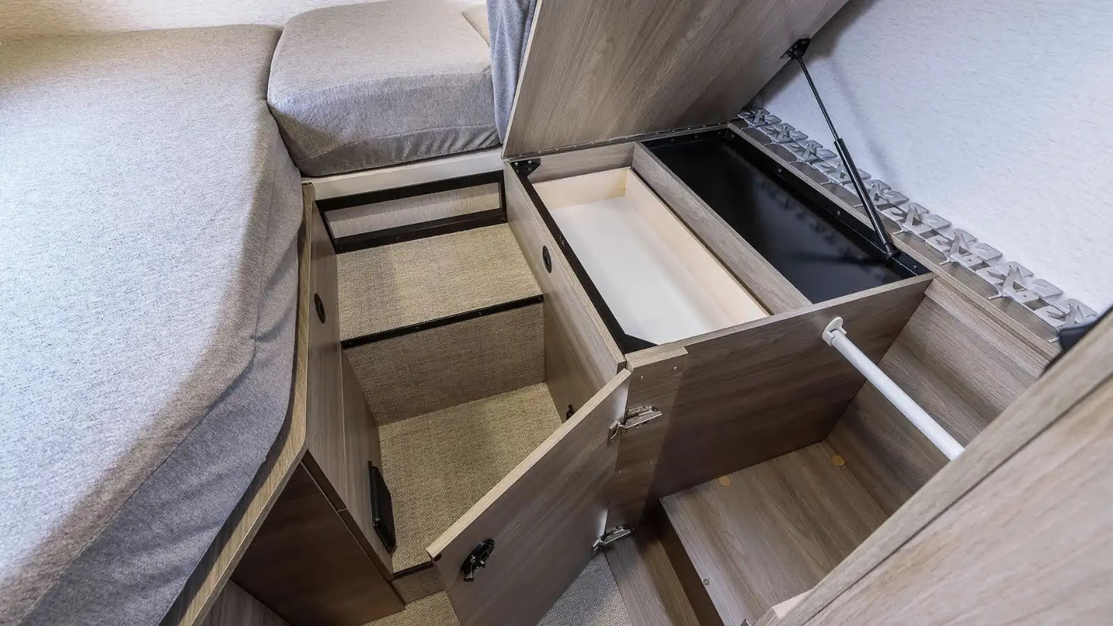 Explore smart under-bed storage in an RV rental. This view shows open wood-grain compartments, a drawer, and a lift-up section.. Winnebago Ekko 2023