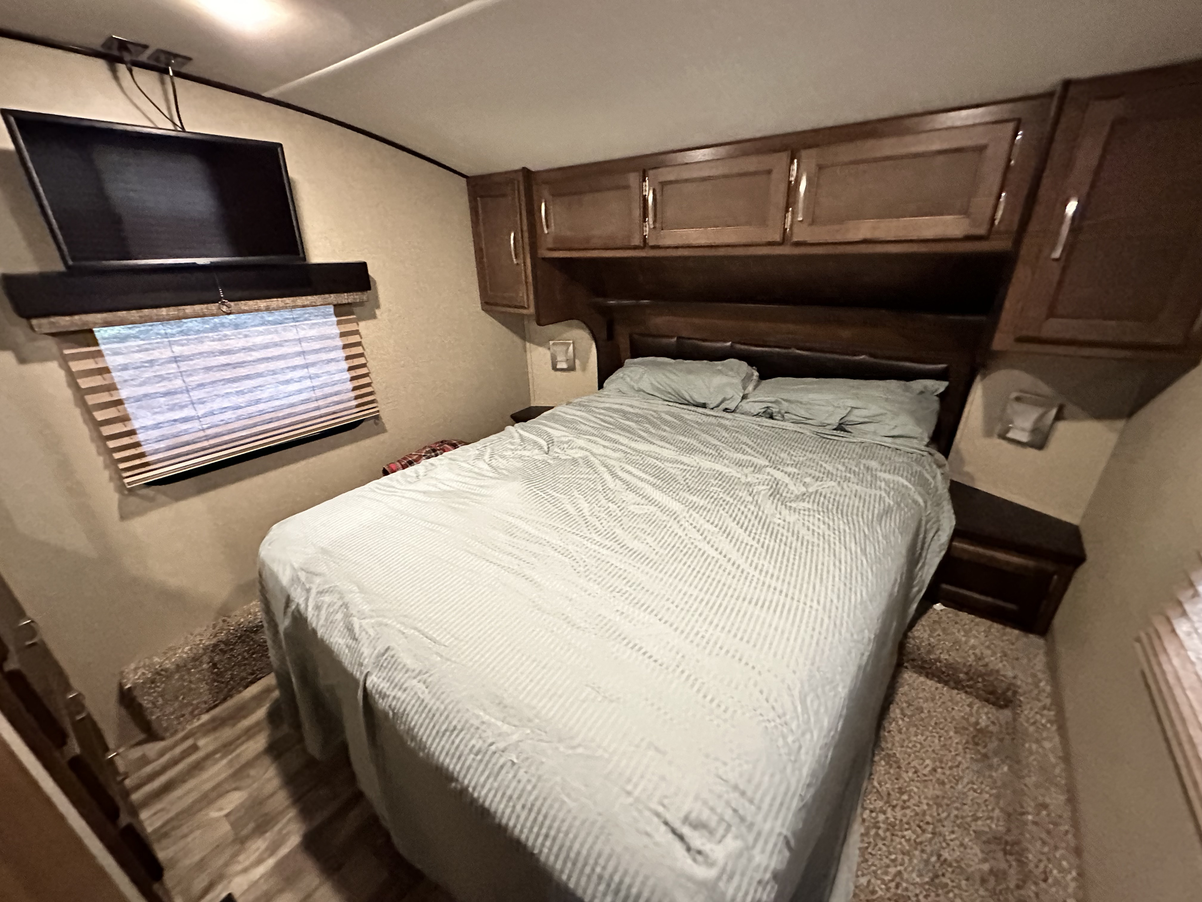 Inside this **rv rental**: a cozy bedroom with light-striped bedding, a TV, and dark wood storage cabinets.. Grand Design Reflection 2018