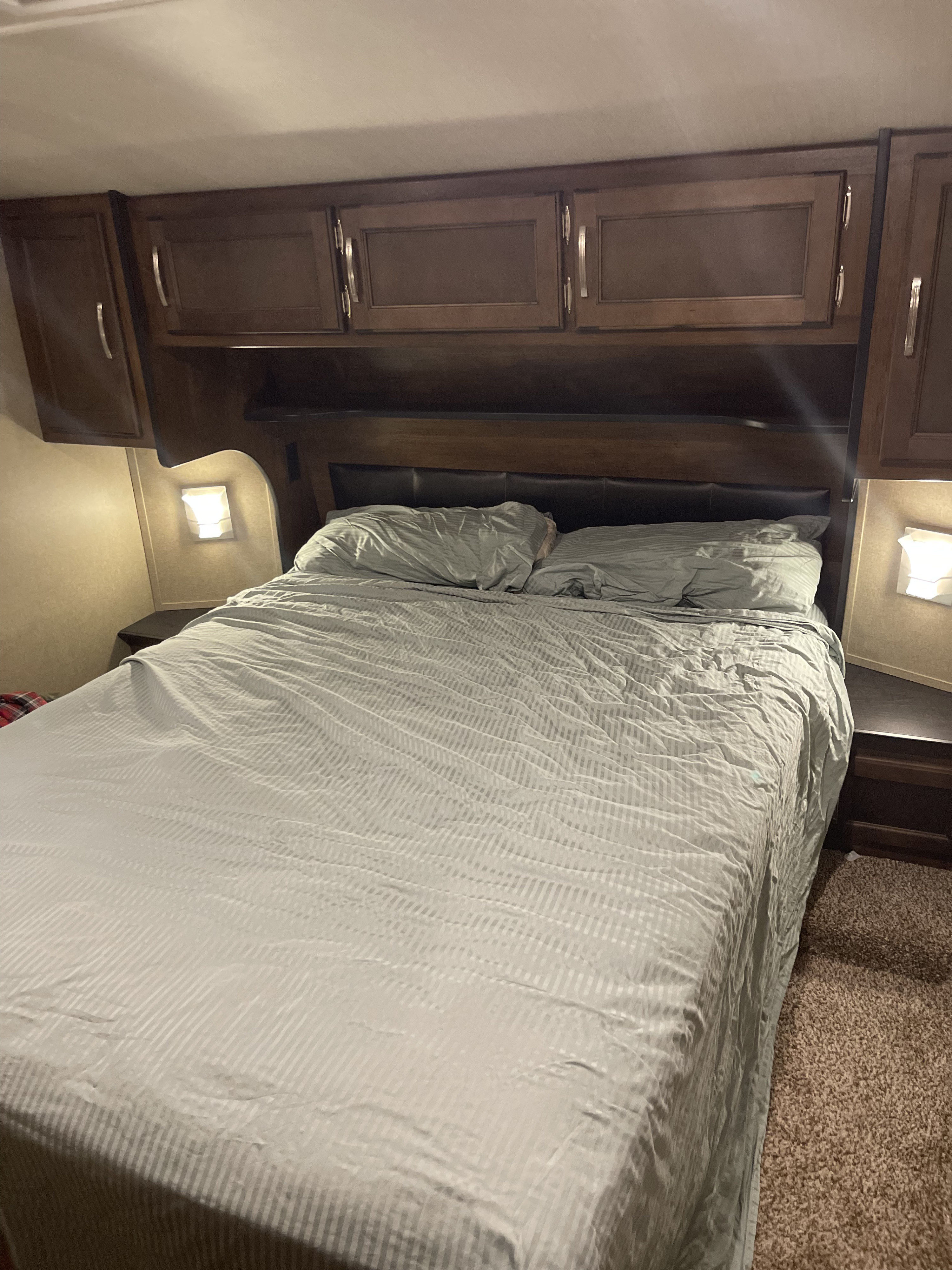 Cozy RV rental bedroom with striped bedding, dark wood cabinets, and bedside lights. Ideal compact travel accommodation.. Grand Design Reflection 2018