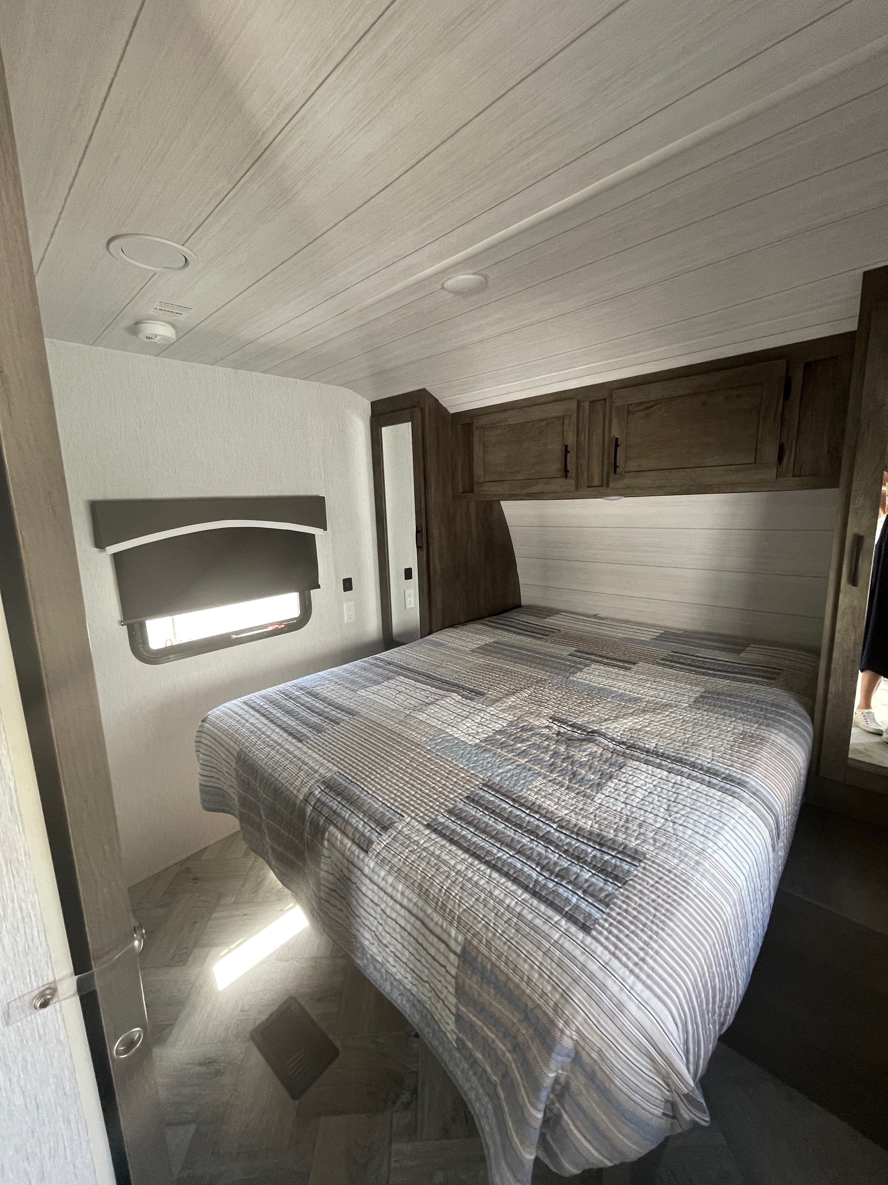 Spacious RV rental bedroom with comfortable bed, overhead cabinets, window, and light wood-planked ceiling.. Forest River Evo T2360 2022