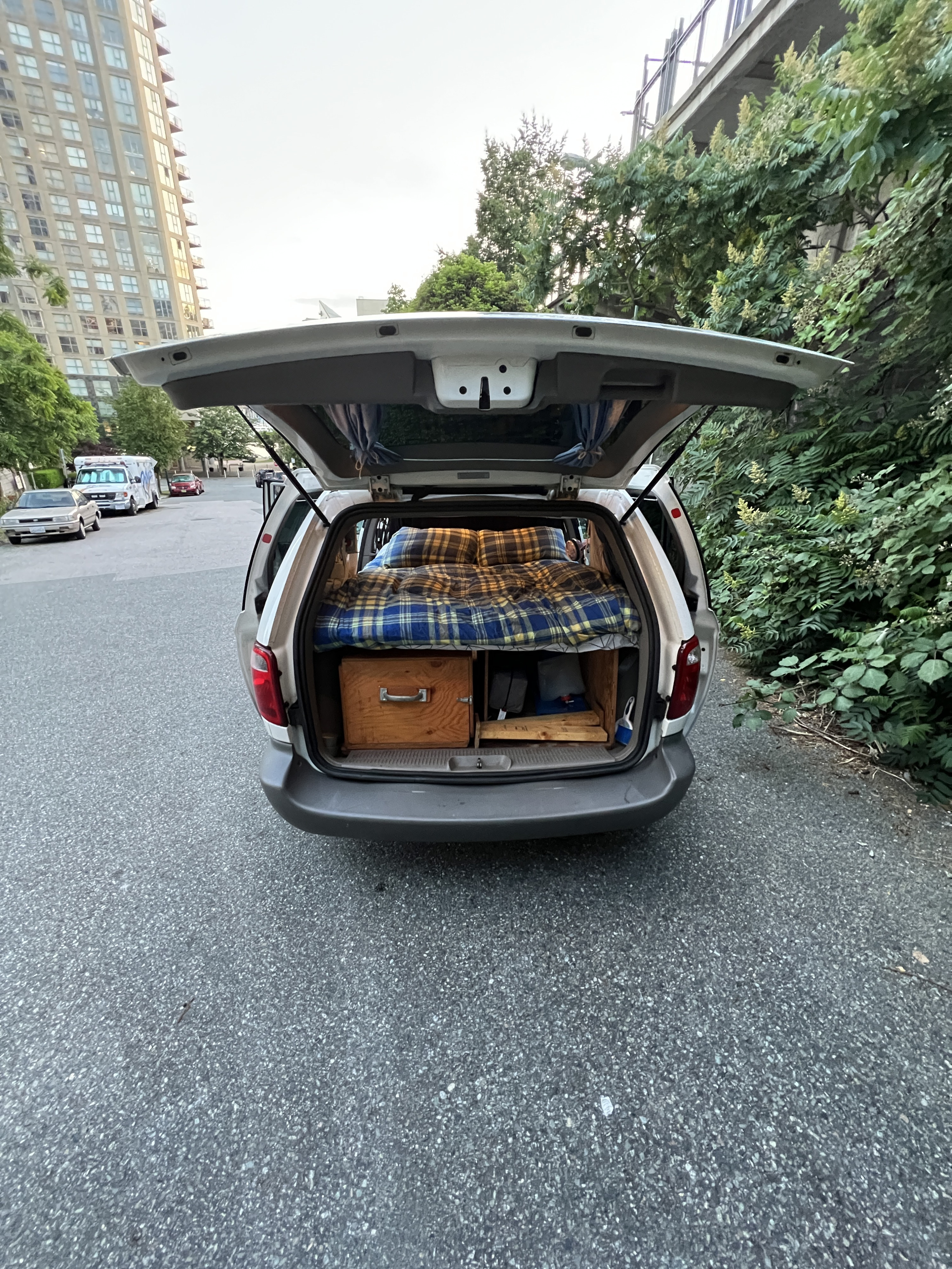 Ready for an RV rental trip! This customized minivan shows its cozy bed and storage setup in the open trunk.. Dodge Caravan 2001
