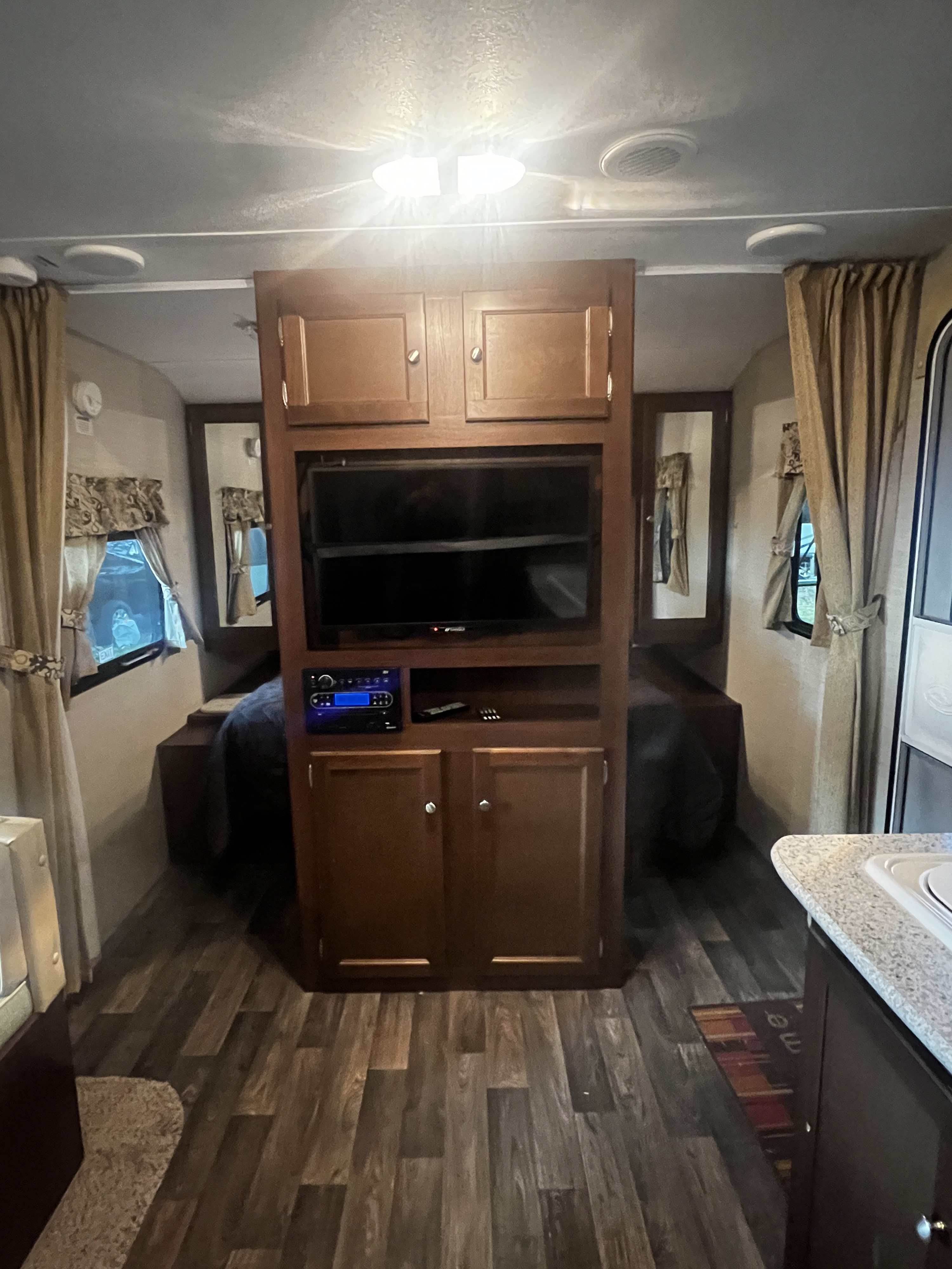 This RV rental showcases a cozy interior with central TV, stereo, bed, brown cabinetry, and wood flooring.. Keystone Bullet 2016