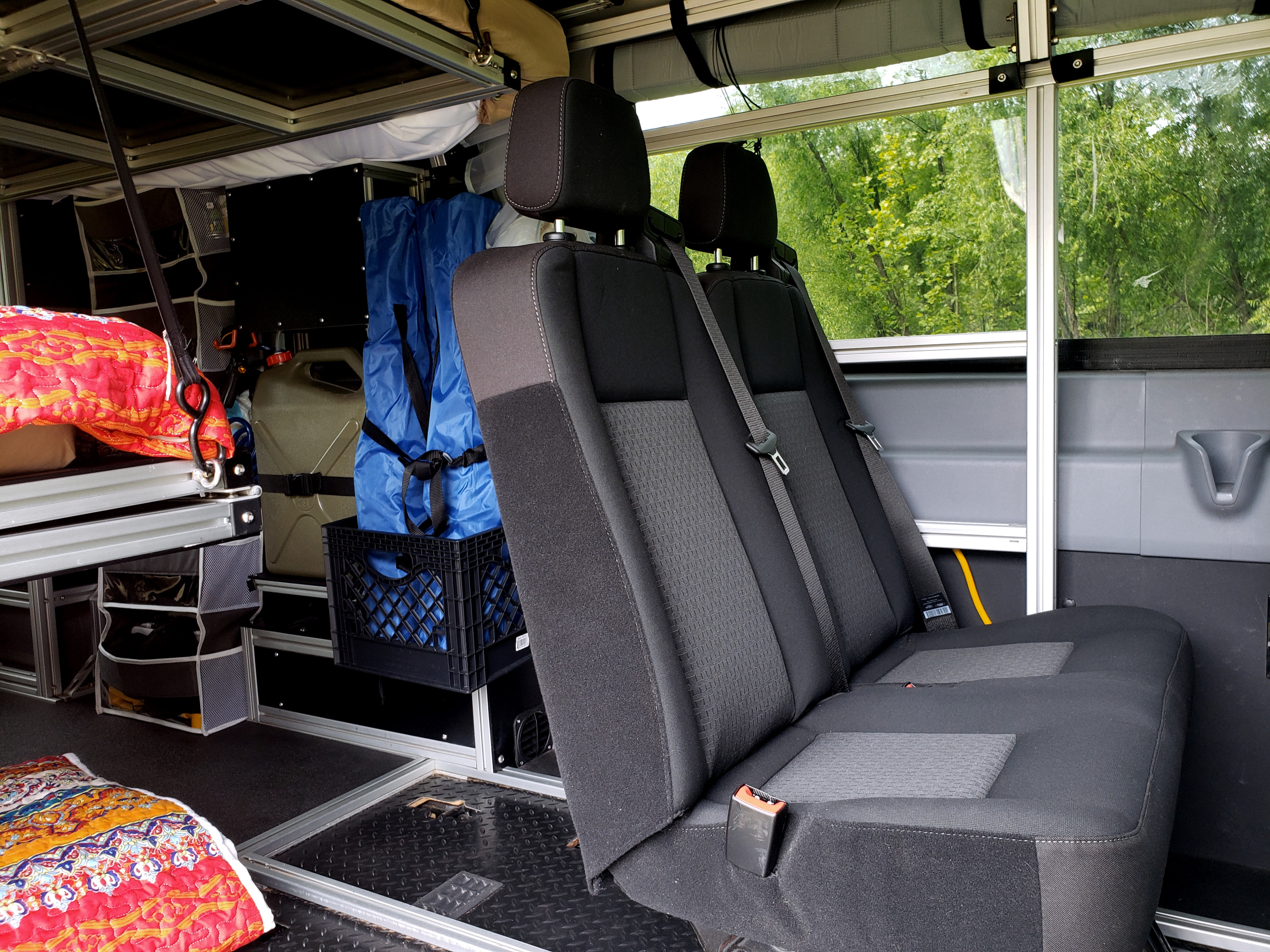 Experience comfort in this RV rental! View of rear seats, modular storage, and a sleeping area in a custom van conversion.. Ford Transit 2019