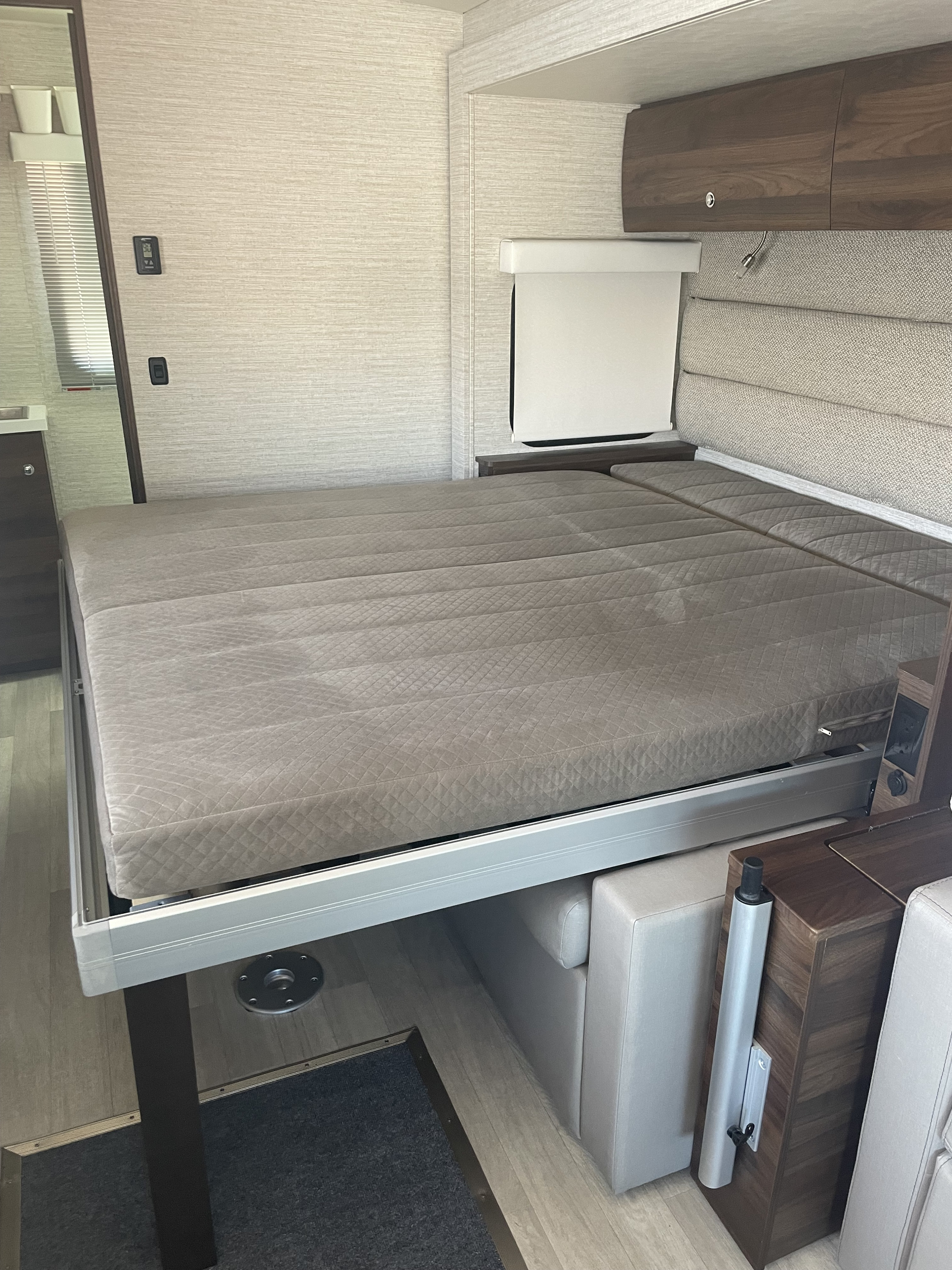 RV rental interior: A compact, quilted bed extends over hidden seating, showcasing smart design for mobile living.. Winnebago Navion 2022