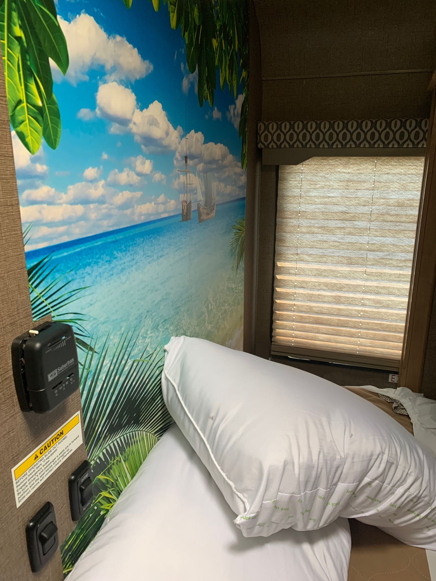 Inside an rv rental, a vibrant tropical beach mural enhances the bedroom. Features a window, pillows, and slide-out controls.. Thor Freedom Elite 2019