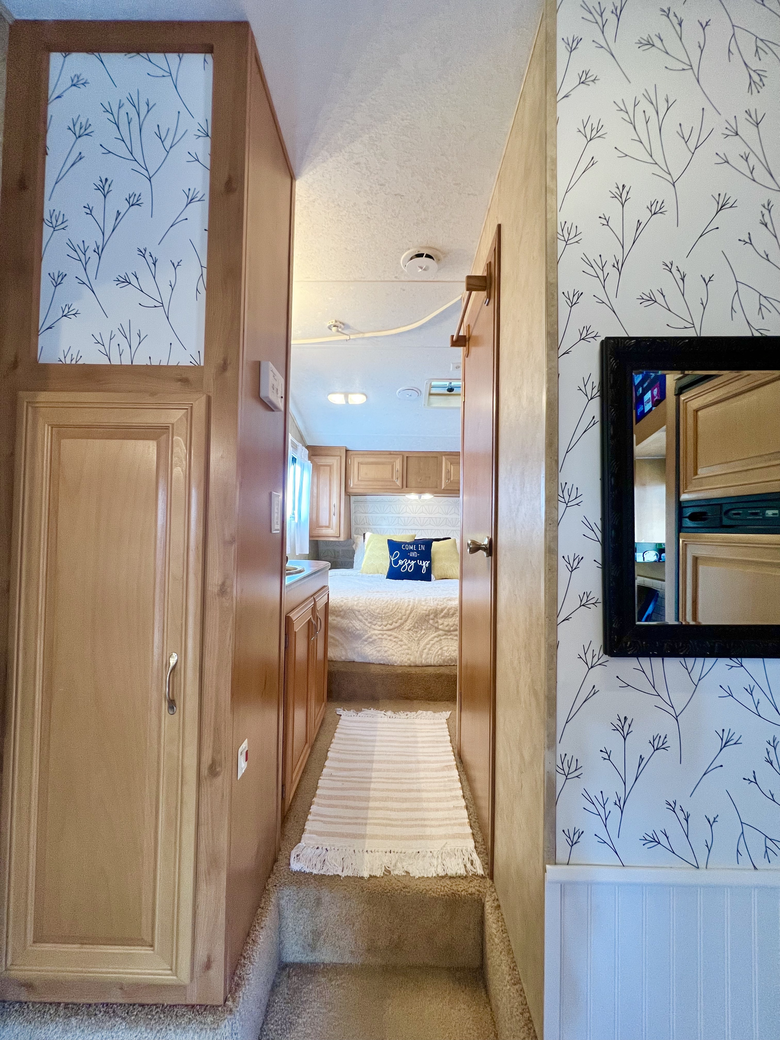 Cozy RV rental interior: hallway with patterned wallpaper leads to a comfortable bedroom. Wood paneling and a mirror add charm.. Keystone RV Raptor Toy Hauler 2007
