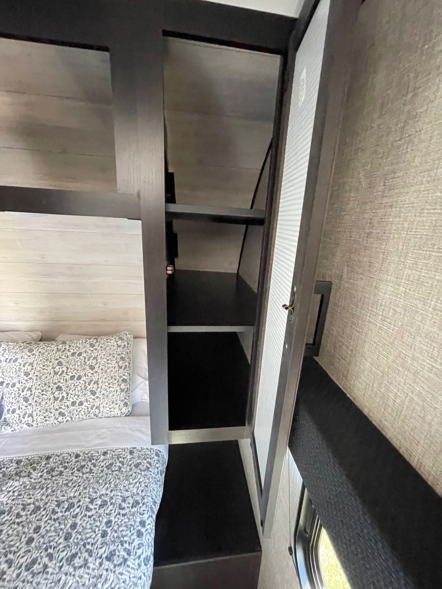 This cozy RV rental features a comfortable bedroom with patterned bedding, open storage, and a small window.. Jayco Jay Flight 2023